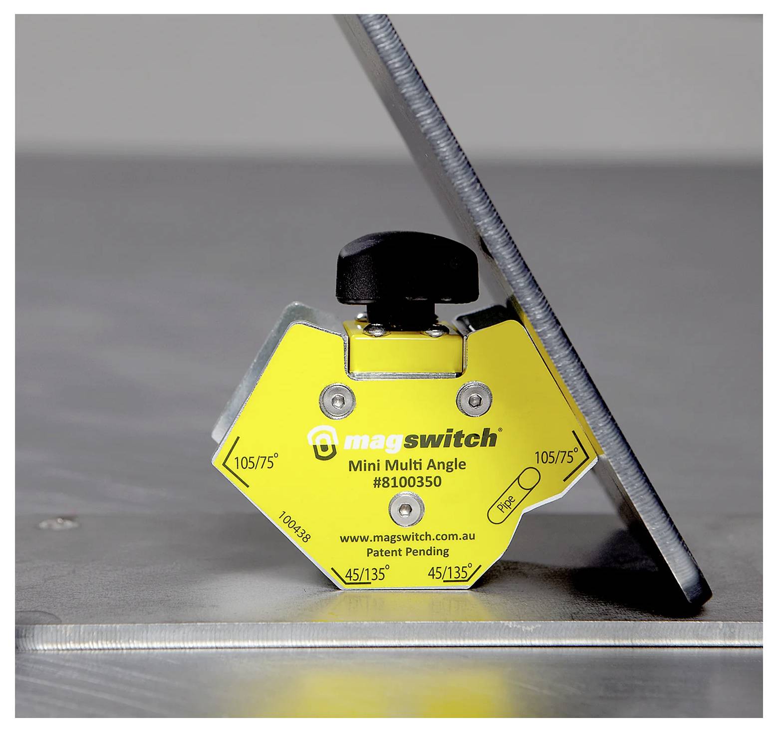 Ein gelber Magswitch Mini Multi Angle Magnet hält ein Metallblech in einem Winkel auf einer metallischen Oberfläche und demonstriert damit seine Funktionalität.