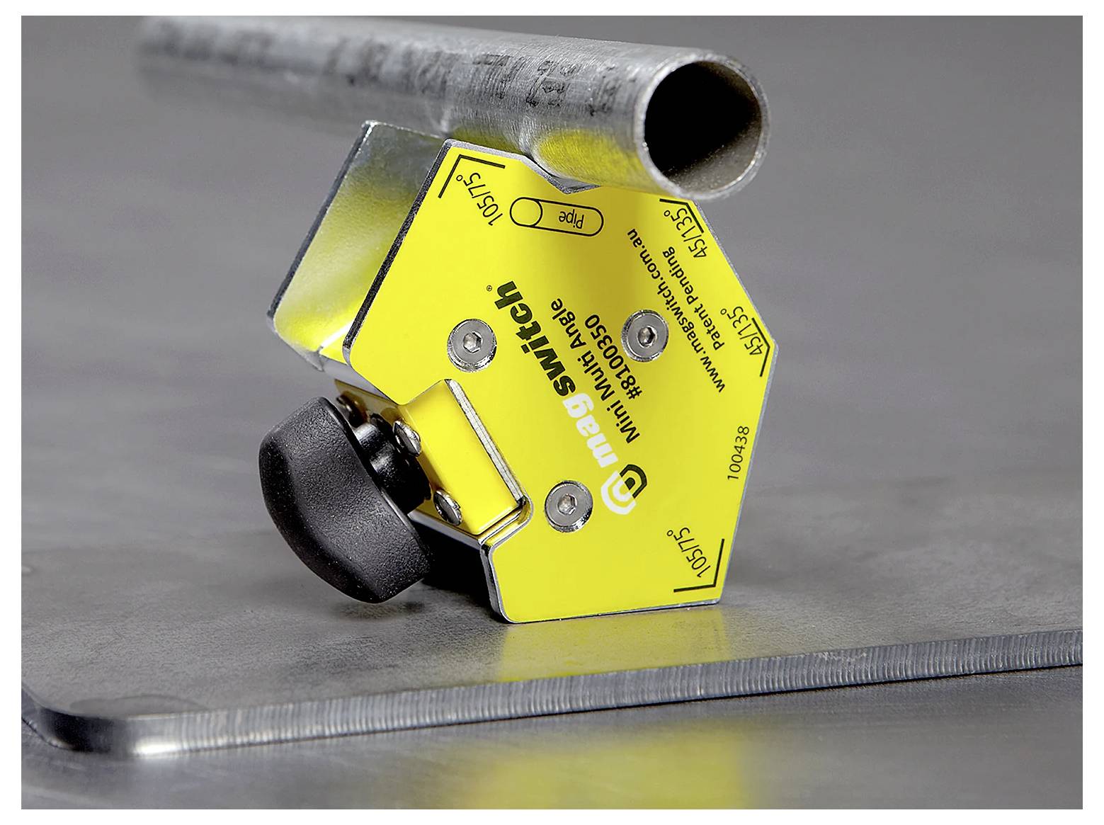 Ein gelber Magnetschalter-Werkzeug, der auf einer Metalloberfläche befestigt ist und ein zylindrisches Metallrohr über einem flachen Blech sichert.