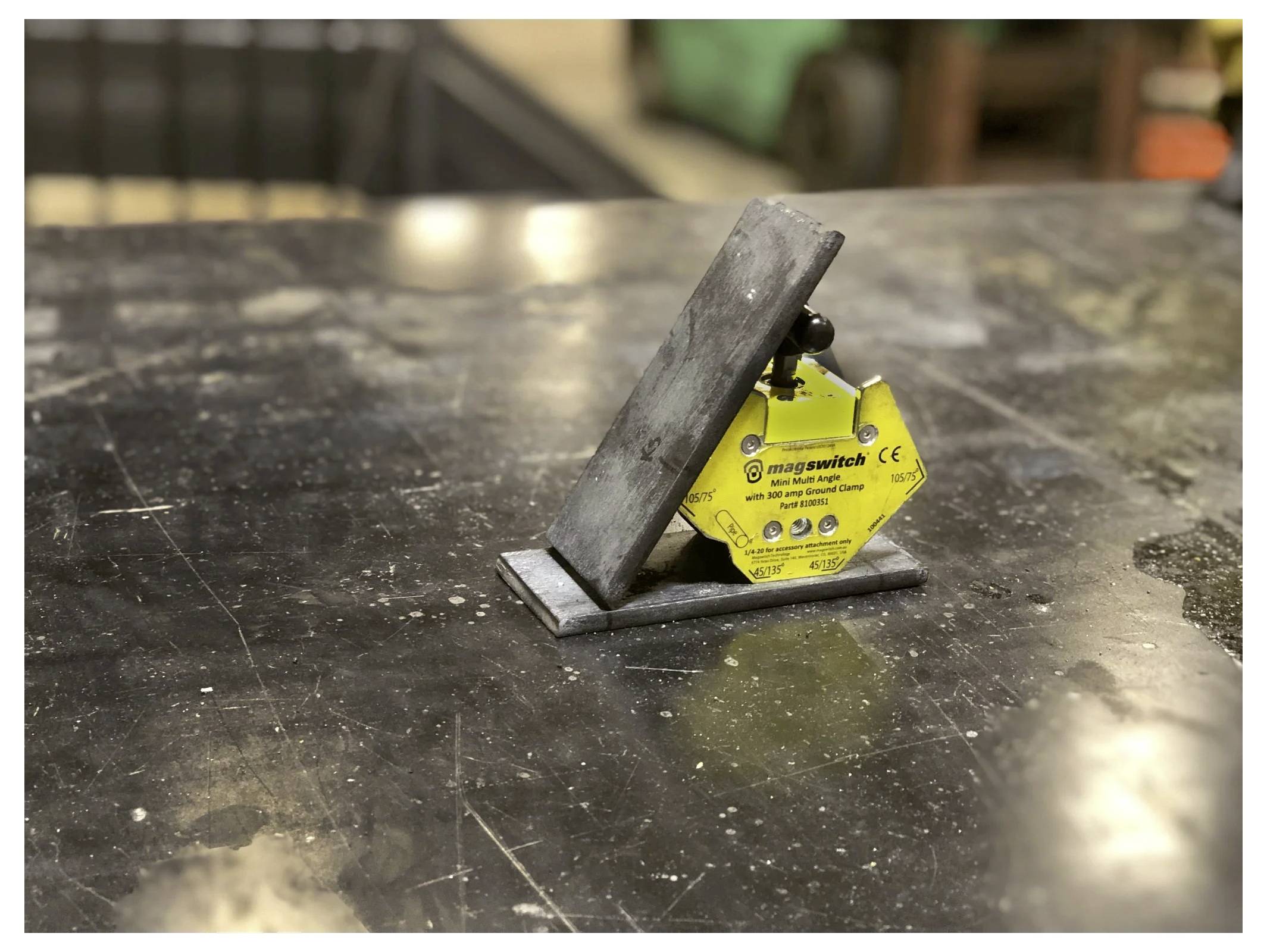 Ein Metallobjekt wird von einem gelben magnetischen Werkzeug mit der Bezeichnung ‚Mag-Schalter' aufrecht auf einem Tisch gehalten. Die Tischoberfläche ist dunkel und glänzend.