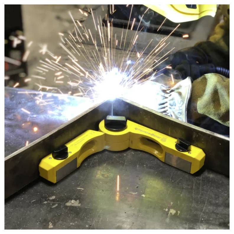 Eine Person schweißt eine Metallverbindung mit einer Ecken-Schweißmagnetklemme in einer Werkstatt, wobei Funken während des Schweißprozesses durch die Luft sprühen.