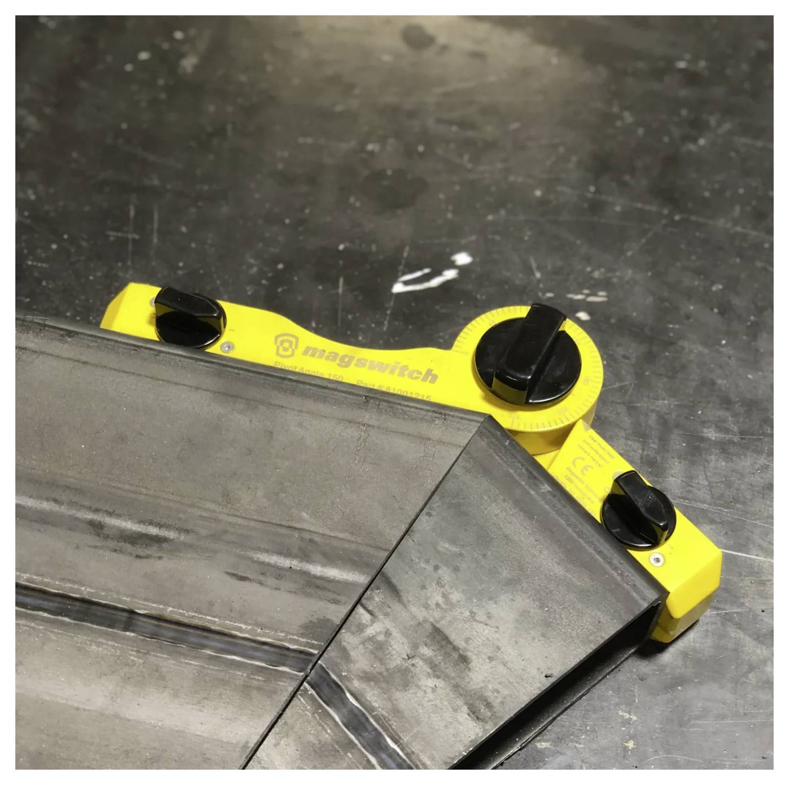 Ein gelbes magnetisches Schweißwinkelwerkzeug befestigt zwei Metallstücke in einem präzisen Winkel auf einer Werkbank.