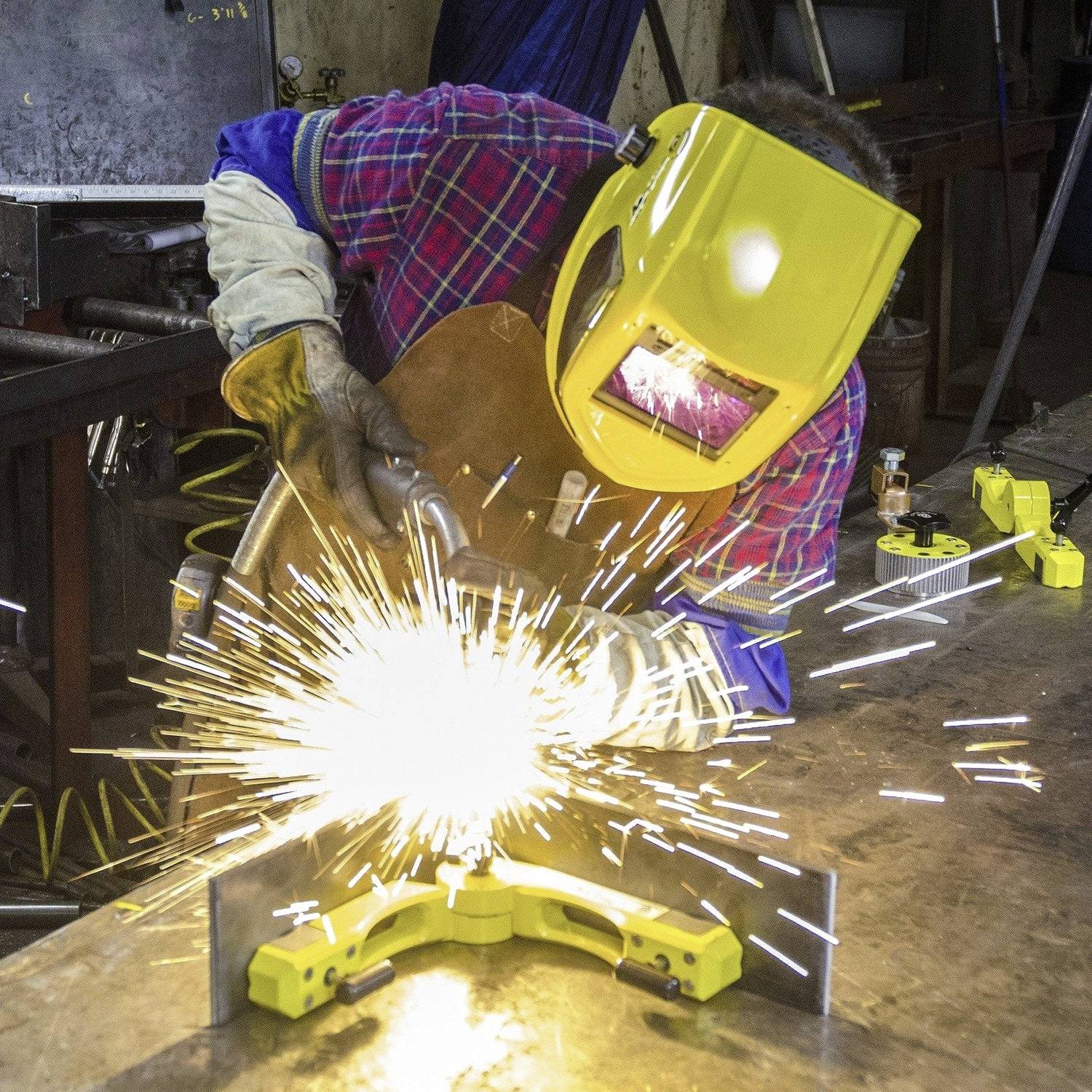 Eine Person schweißt Metallteile in einer Werkstatt zusammen und trägt einen Schutzhelm und Handschuhe. Helle Funken sind sichtbar.