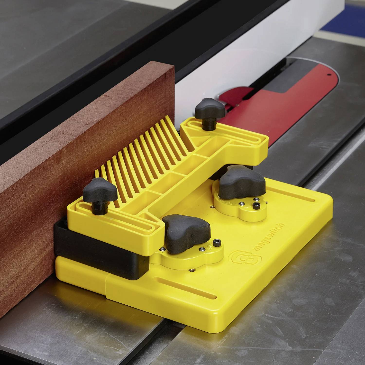 Ein gelbes Sägeblatt-Zubehör mit Knöpfen und einer kammartig geformten Führung ist an einem Sägetisch befestigt und leitet ein Holzstück für einen sicheren Schnitt.