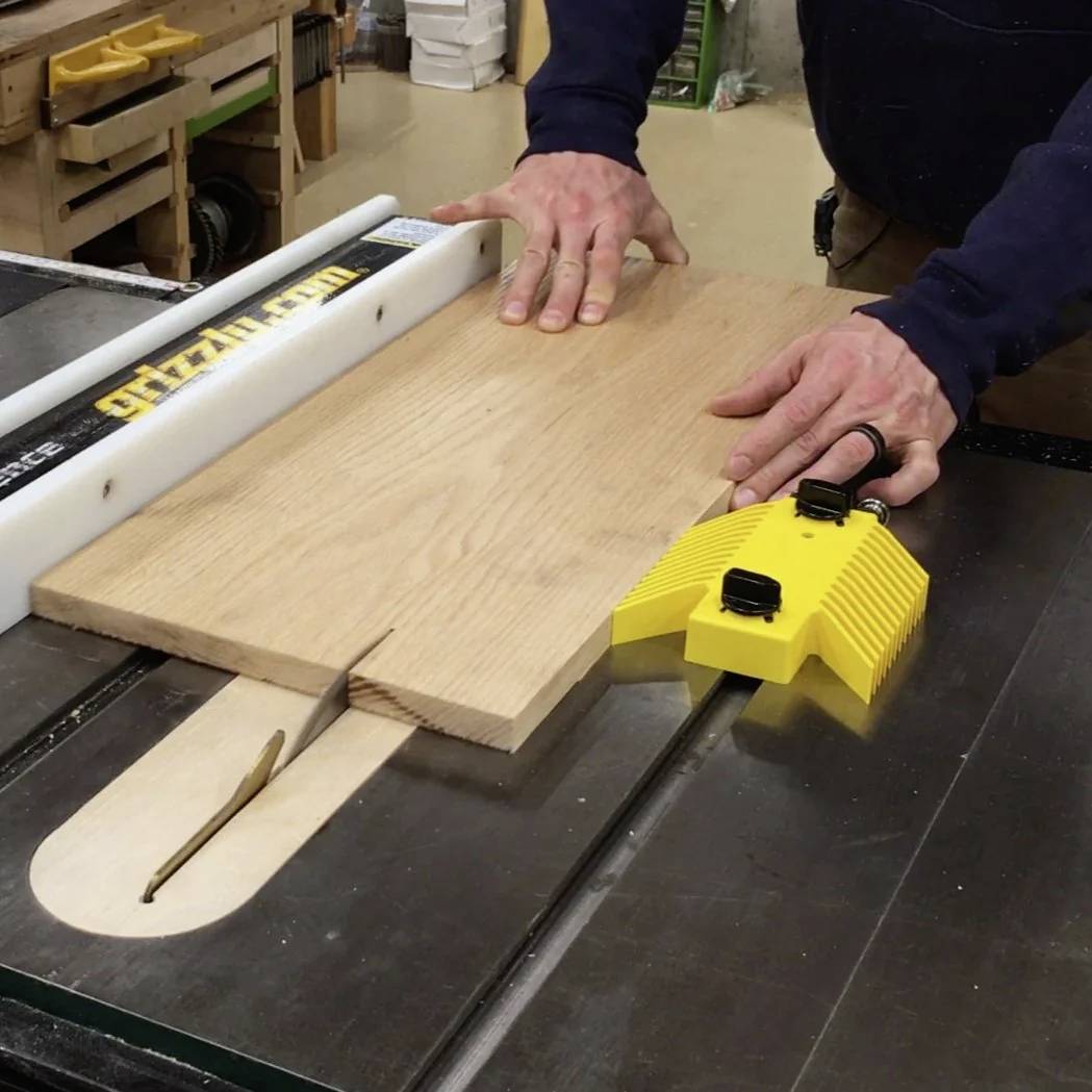 Eine Person bedient eine Kreissäge und führt ein Holzbrett mit Sicherheitsausrüstung durch die Sägeblatt, wobei Holzbearbeitung in einer Werkstattumgebung demonstriert wird.