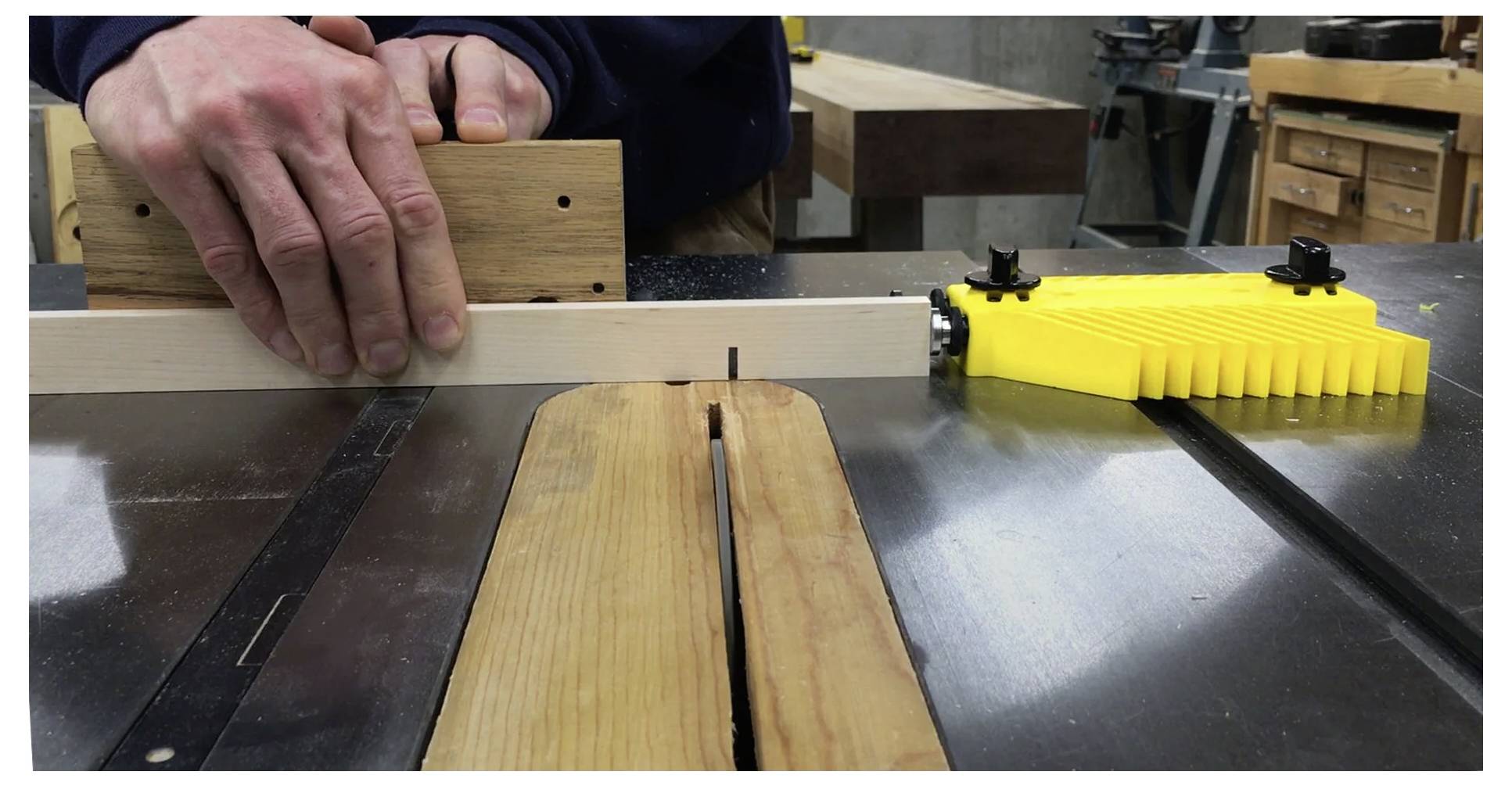 Eine Person schneidet ein Stück Holz mit einer Kreissäge. Hände führen das Holz durch die Säge, wobei gelbe Sicherheitsvorrichtungen sichtbar sind.