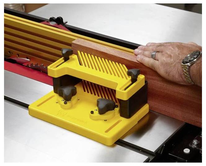 Eine Person, die ein gelbes Führungsbrett (Featherboard) verwendet, um ein Holzstück an einer Kreissäge zu führen und dabei Sicherheit und Präzision beim Schneiden zu gewährleisten.