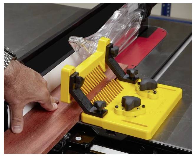 Eine Hand, die einen gelben Schubblock verwendet, um ein Holzbrett durch eine Kreissäge zu führen und eine sichere Holzbearbeitungstechnik zu demonstrieren.