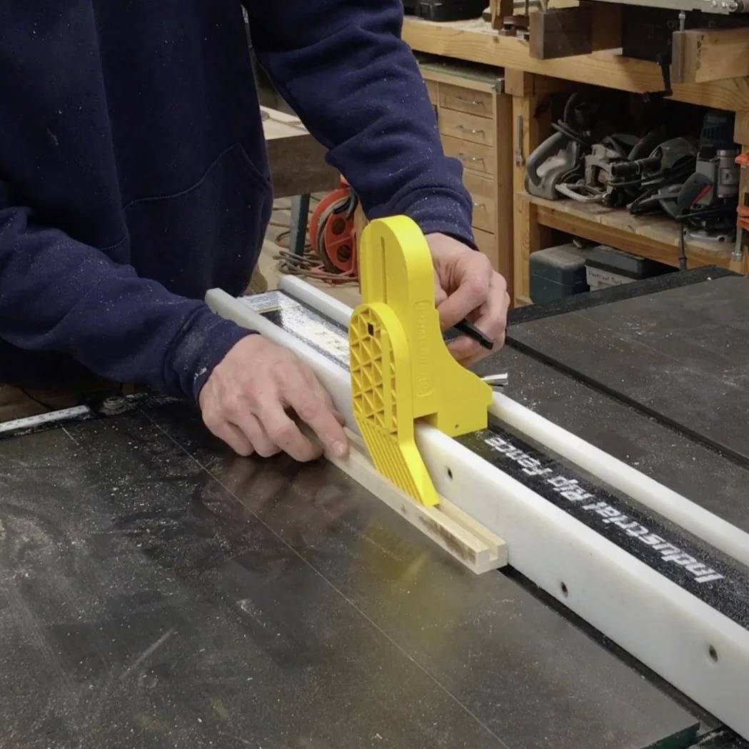 Ein Mitarbeiter verwendet einen gelben Schubblock, um Holz an einer Kreissäge für präzises Schneiden in einer Werkstatt zu führen.