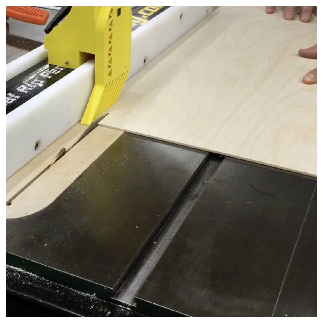 Eine Kreissäge, die ein Holzbrett schneidet, geführt von einem gelben Schubblock, mit Händen, die die Bewegung des Brettes vorsichtig kontrollieren.