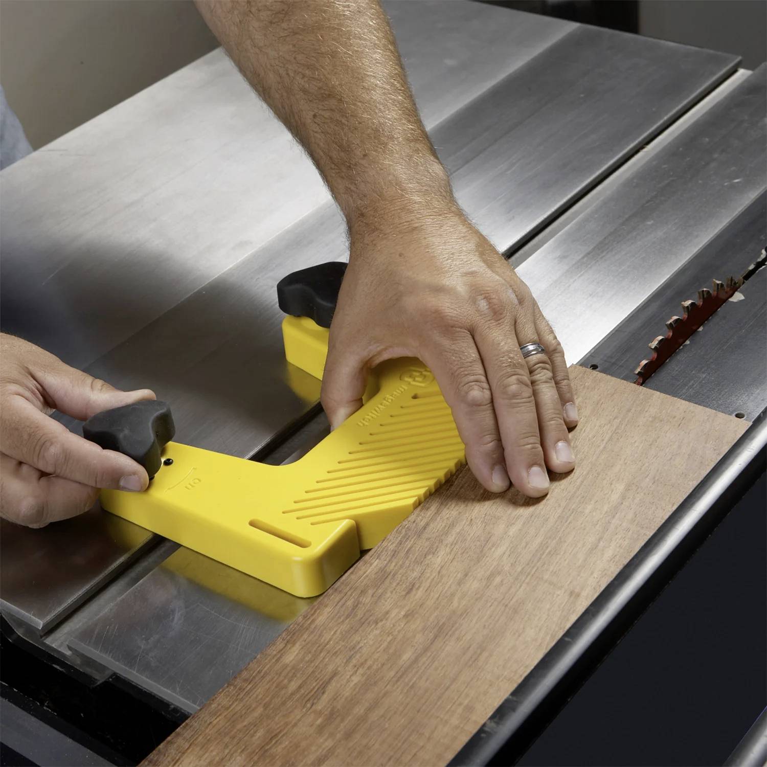 Eine Person verwendet einen gelben Schubblock, um ein Holzbrett sicher durch eine Tischkreissäge zu führen und dabei die Handsicherheit während des Schneidvorgangs zu gewährleisten.