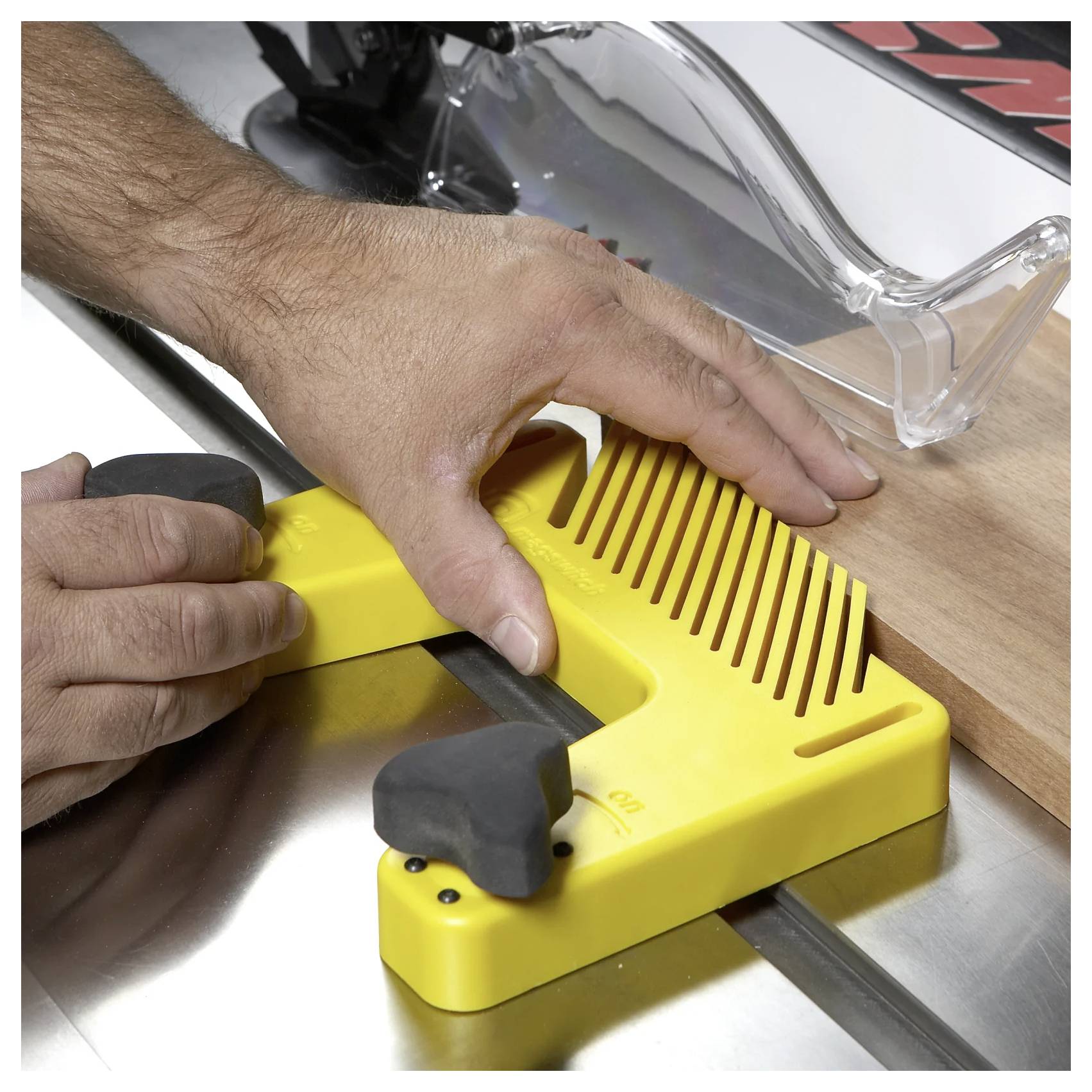 Eine Hand einer Person justiert eine gelbe Kunststoff-Sicherheitsvorrichtung an einer Kreissäge und stellt sicher, dass Holz sicher geschnitten wird. Der durchsichtige Sägeschutz ist sichtbar.