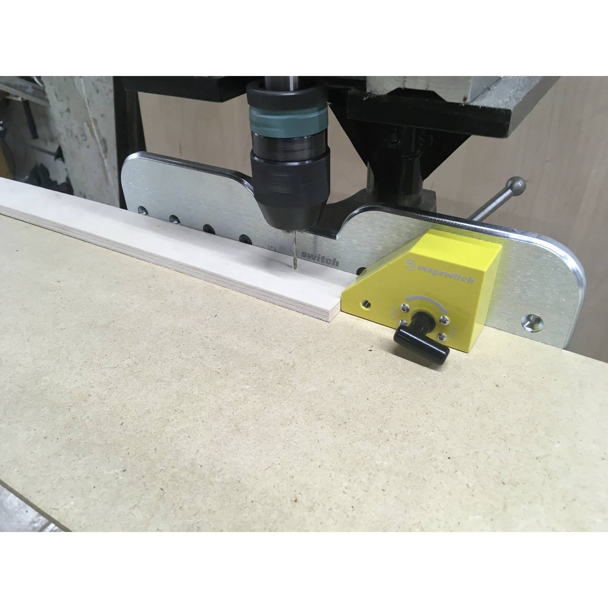 Eine Säulenbohrmaschine mit montierter Sicherheitsvorrichtung wird verwendet, um präzise ein Loch in eine Holzplatte zu bohren und damit die Präzision der Holzbearbeitung zu demonstrieren.