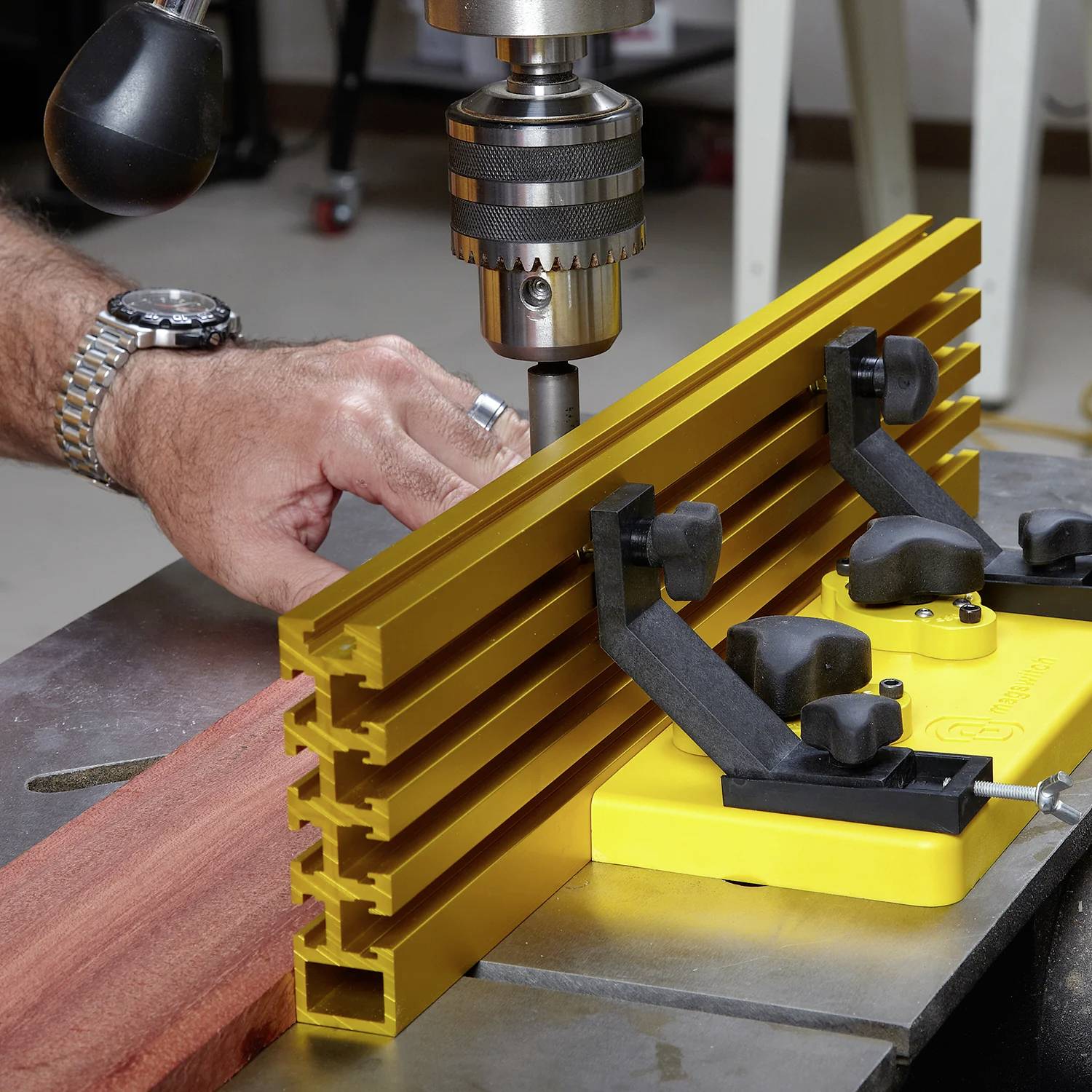 Eine Person justiert eine Holzbearbeitungsbohrmaschine, wobei eine gelbe V-Block-Klemme ein Holzstück sicher an seinem Platz hält, um präzises Bohren zu ermöglichen.