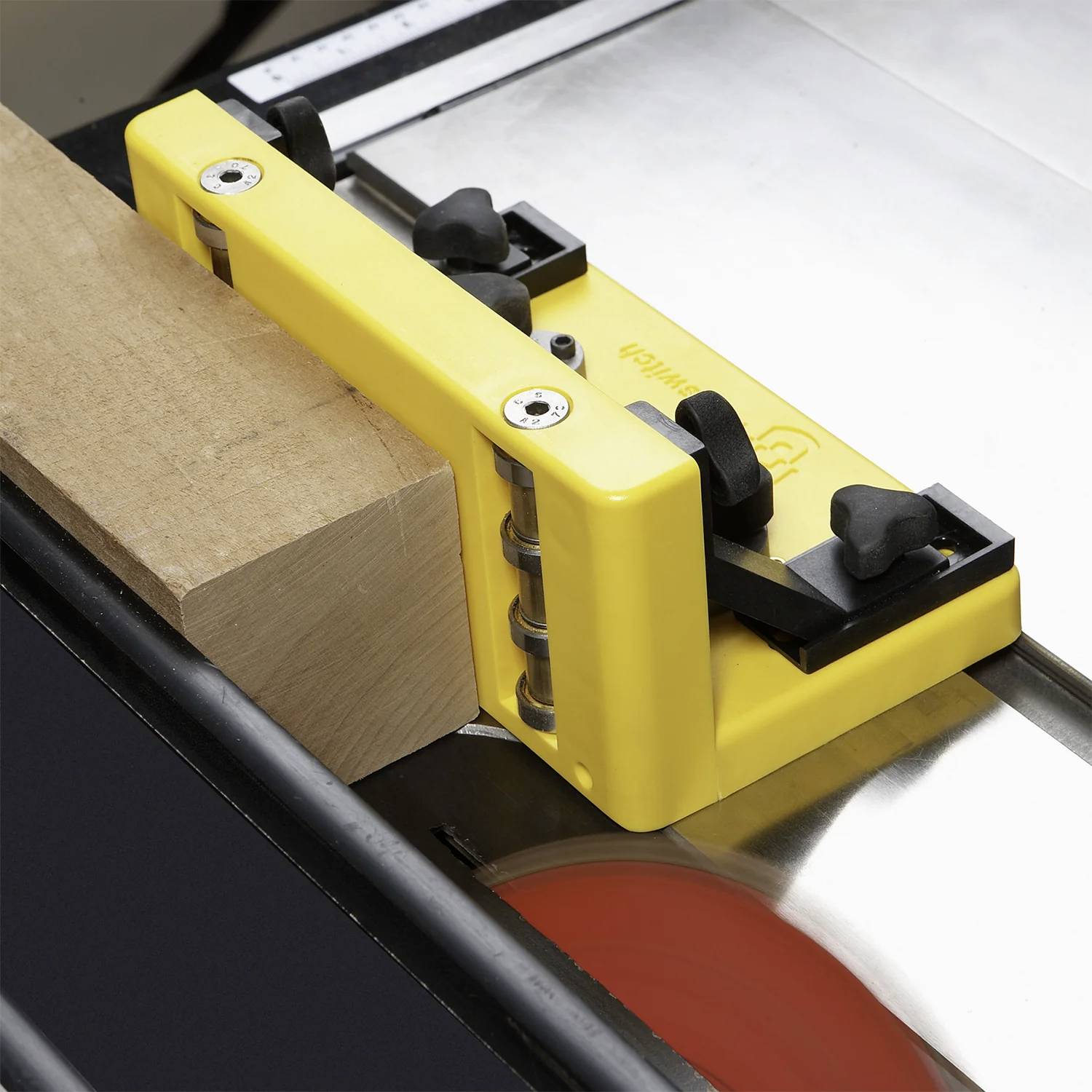 Ein Kreissägetisch mit einer gelben Schutzhaube ist neben einem Holzblock positioniert, was sichere Schneidpraktiken demonstriert.