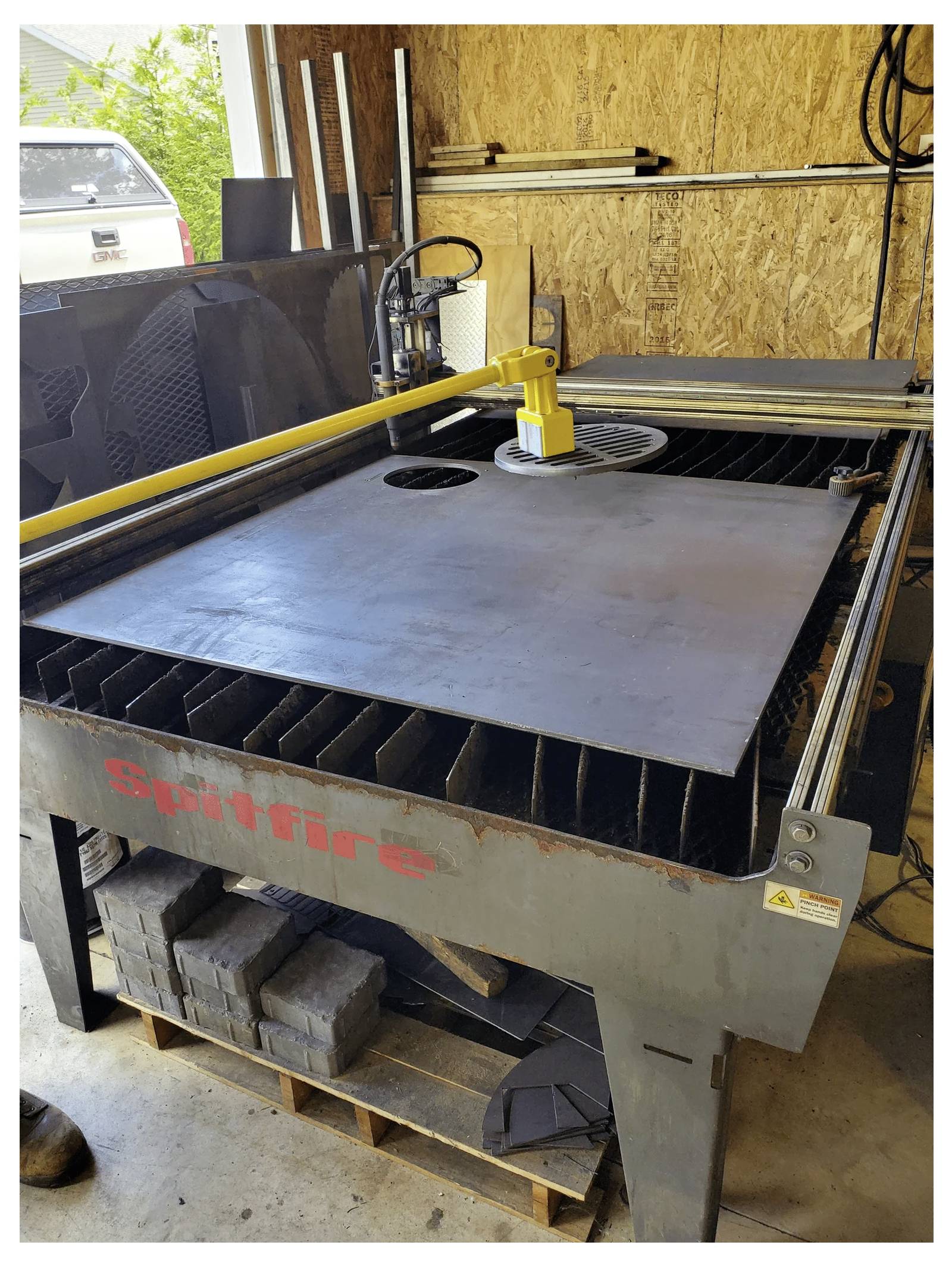 Industrielle Schneidemaschine in einer Werkstatt mit einer großen Metallplatte, die unter einem gelben Arm zum Schneiden positioniert wird, mit der Bezeichnung Spitfire.