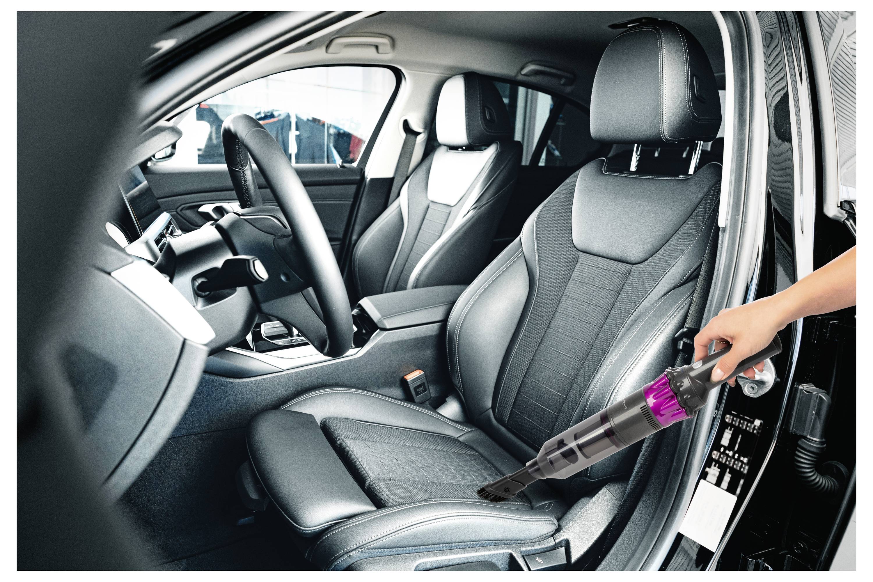Eine Person verwendet einen tragbaren Staubsauger, um den vorderen Beifahrersitz zu reinigen und sich dabei auf den Sitzkissen und den umliegenden Bereich zu konzentrieren.