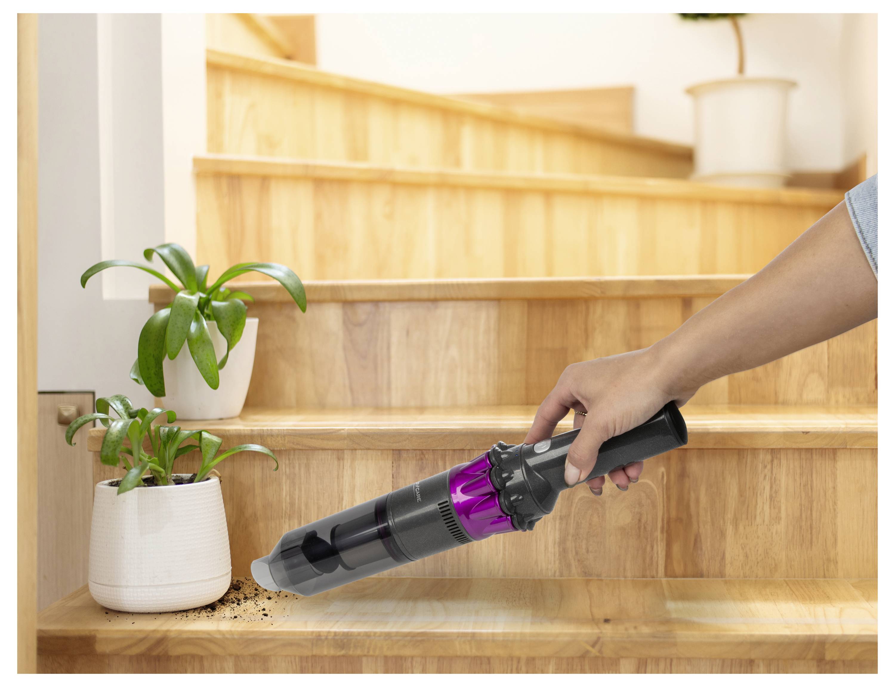 Eine Person benutzt einen tragbaren Staubsauger, um Schmutz zu entfernen, der in der Nähe einer kleinen Pflanze auf Holztreppen verschüttet wurde.