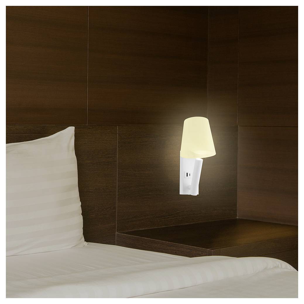 Eine matt beleuchtete beige Lampe ist über einem weißen Kissen und Bettwäsche an einer dunklen Holzwand befestigt und schafft eine ruhige und gemütliche Atmosphäre.