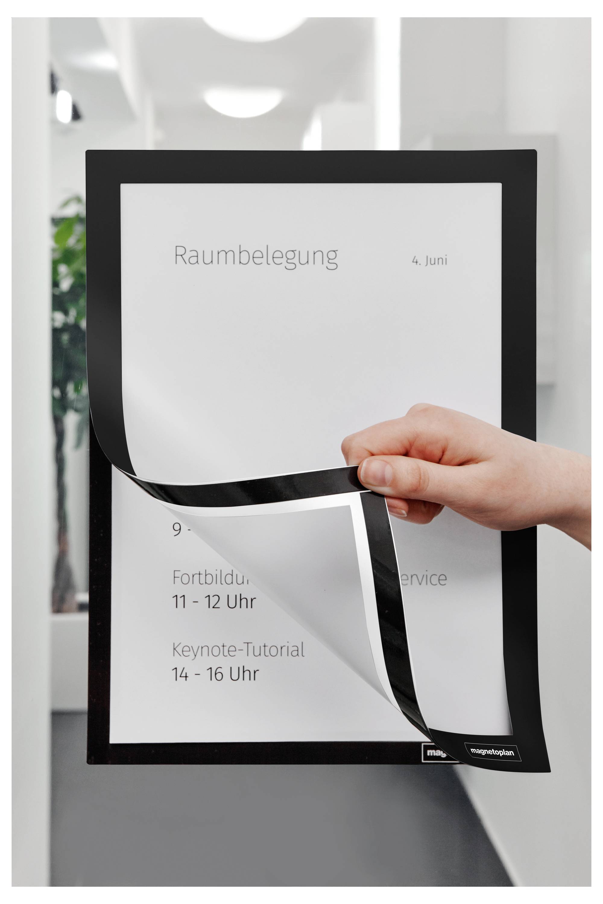 Eine Hand, die ein Schild mit folgendem Text hält: 'Raumbelegung 4. Juni. Fortbildung: 9 - 11 Uhr, Interner Service: 11 - 12 Uhr, Keynote-Tutorial: 14 - 16 Uhr.'