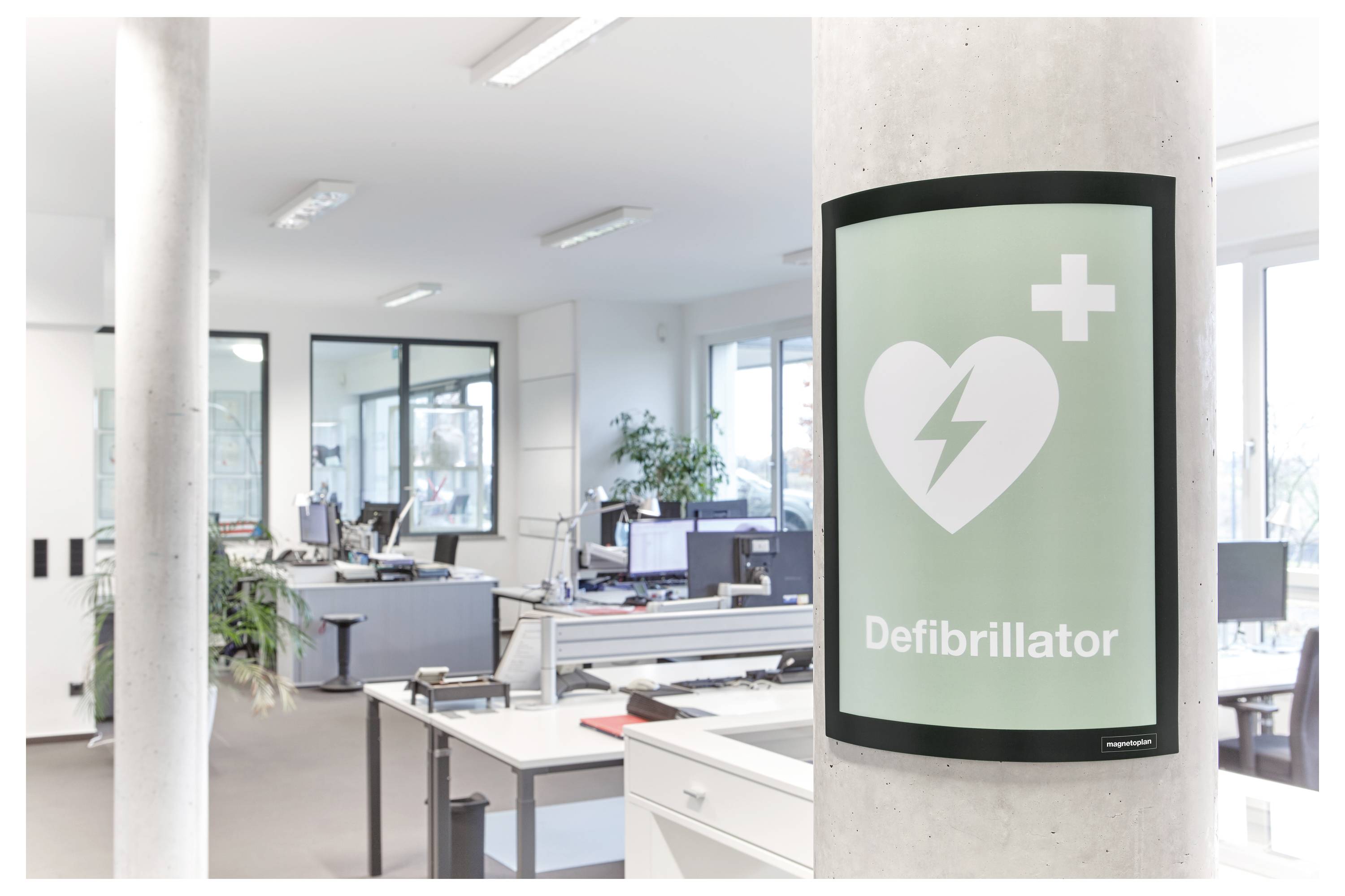 Ein Schild im Büro zeigt ein Herz mit einem Blitz und einem Pluszeichen, beschriftet mit „Defibrillator