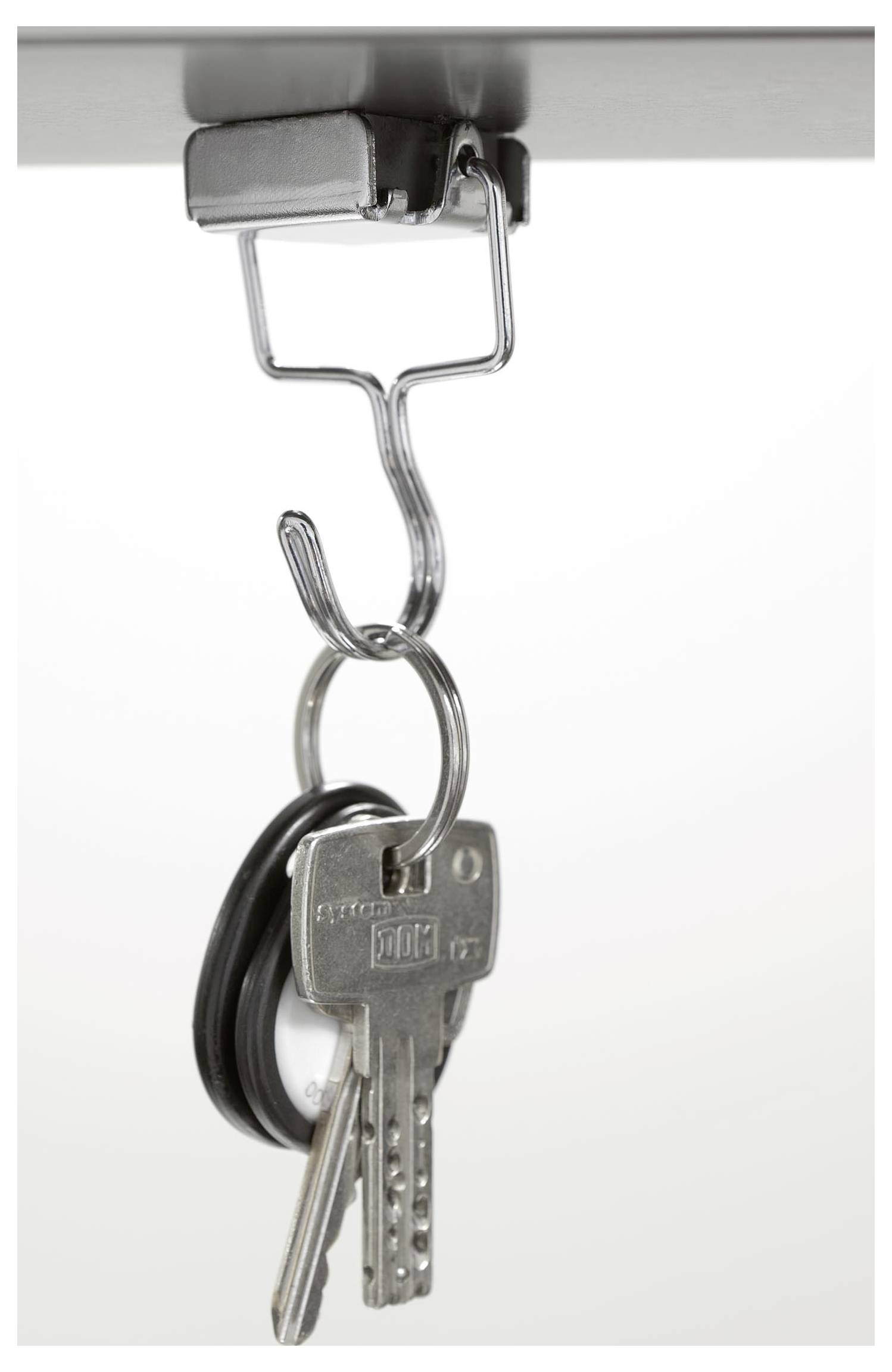 Schlüssel, die an einem Metallhaken hängen, befestigt unter einer Oberfläche, vor einem einfarbigen Hintergrund.