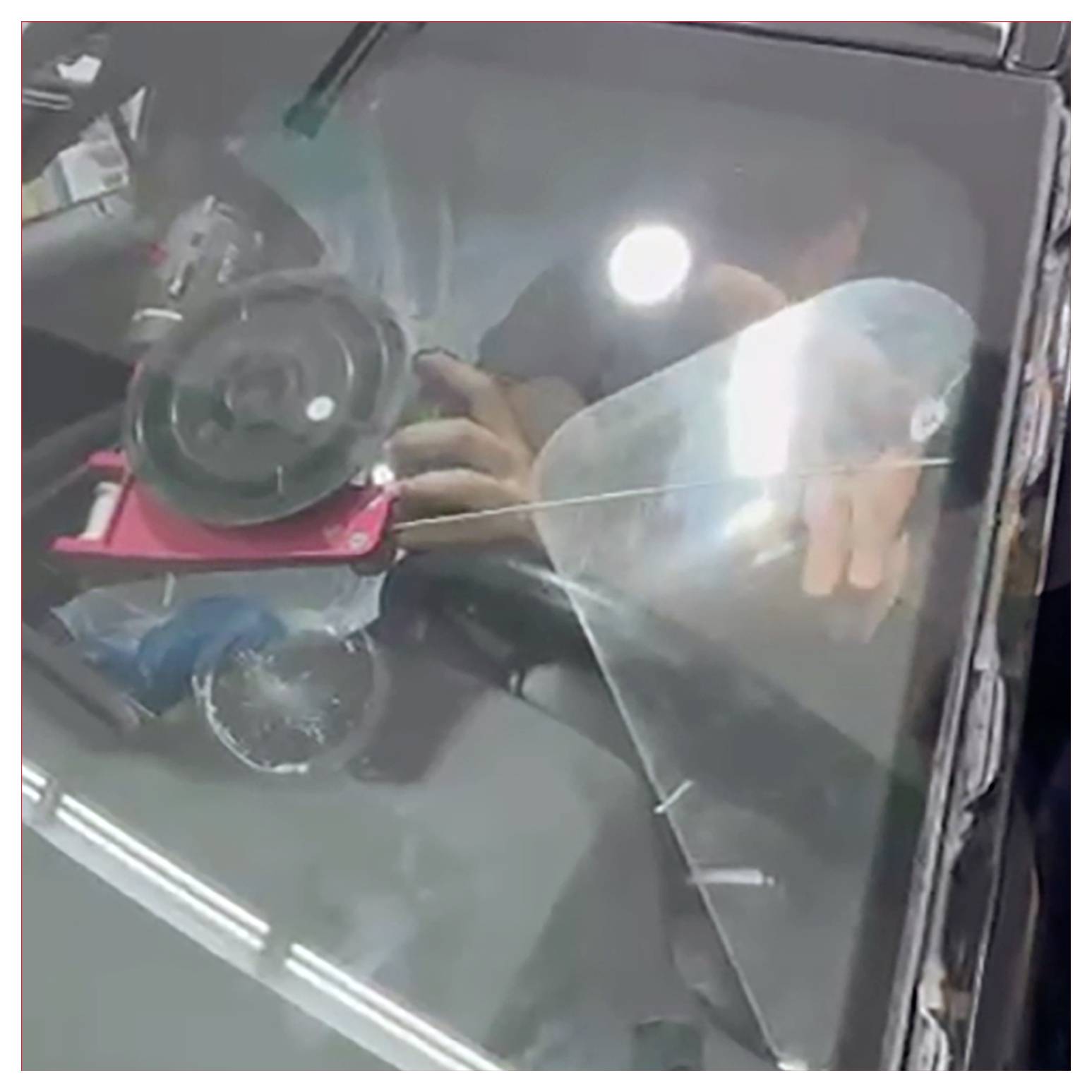 Eine Person, die ein Werkzeug benutzt, um einen Riss in der Windschutzscheibe eines Autos zu reparieren. Die Reflexion und das Licht erzeugen Blendeffekte auf dem Glas.