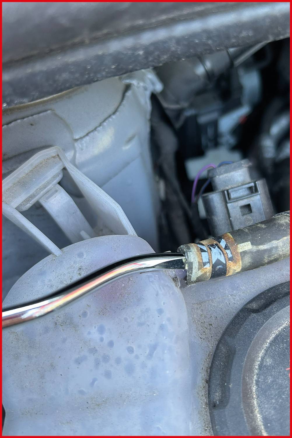 Eine Nahaufnahme eines Automobilmotorenbauteils, die ein angeschlossenes Kabel und ein Plastikteil zeigt, was auf einen Wartungs- oder Reparaturkontext hinweist.