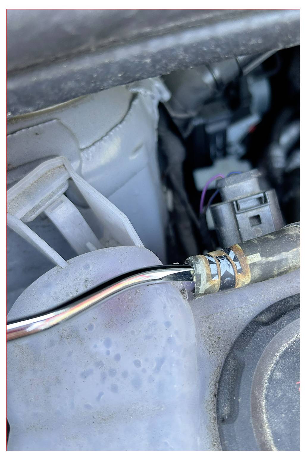 Nahaufnahme einer Motorkomponente mit einem Anschluss an einem Zylinder, die Metall- und Kunststoffteile zeigt.