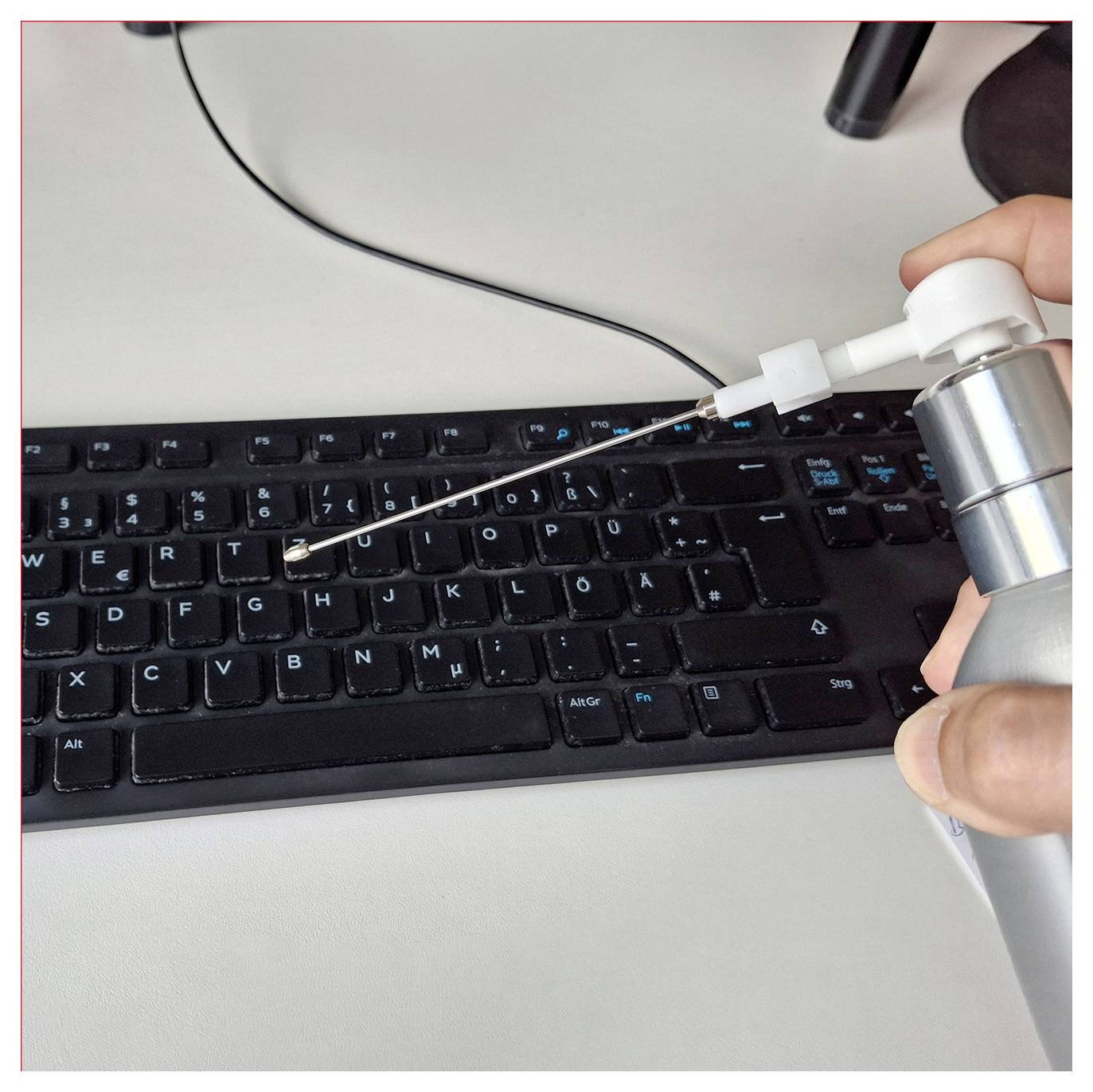 Eine Dose mit Druckluft wird verwendet, um Staub von einer Computertastatur zu entfernen. Die Düse wird zwischen die Tasten gerichtet.