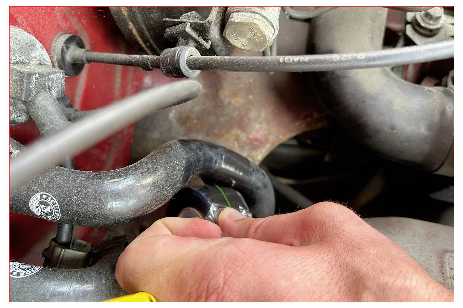 Eine Hand, die einen schwarzen Deckel auf einem Fahrzeug-Motorschlauch dreht, umgeben von verschiedenen verbundenen Schläuchen und Metallteilen, was auf Wartungsarbeiten hinweist.