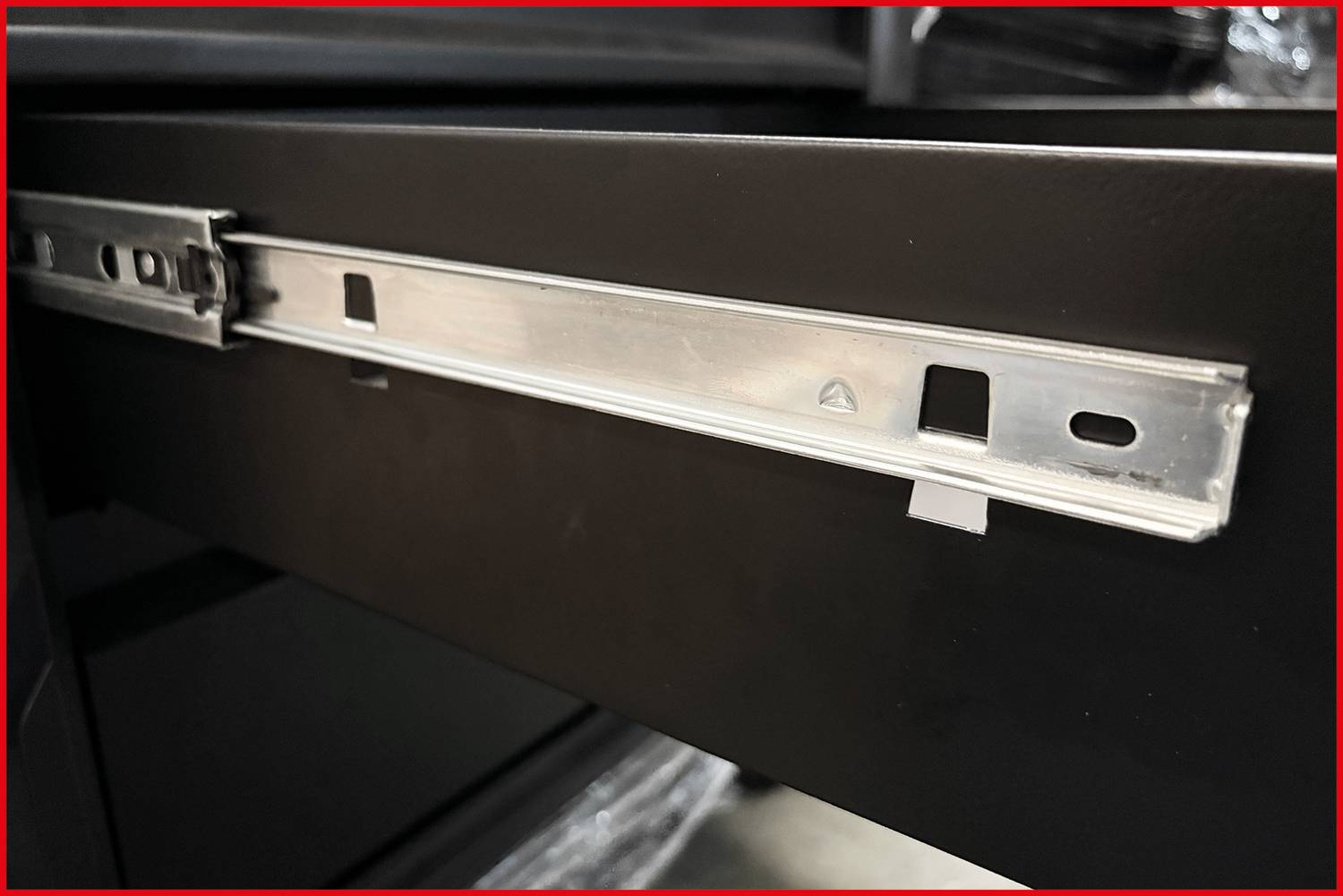 Eine Nahaufnahme einer Metallschienenmechanik auf einer teilweise geöffneten schwarzen Holzschublade, die das glatte Gleitsystem im Inneren des Schranks zeigt.