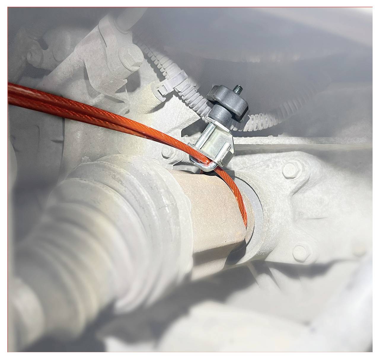 Eine Nahaufnahme eines roten Kabels, das von einer Klemme an einer Metallkomponente gehalten wird, möglicherweise Teil eines mechanischen Systems eines Fahrzeugs.