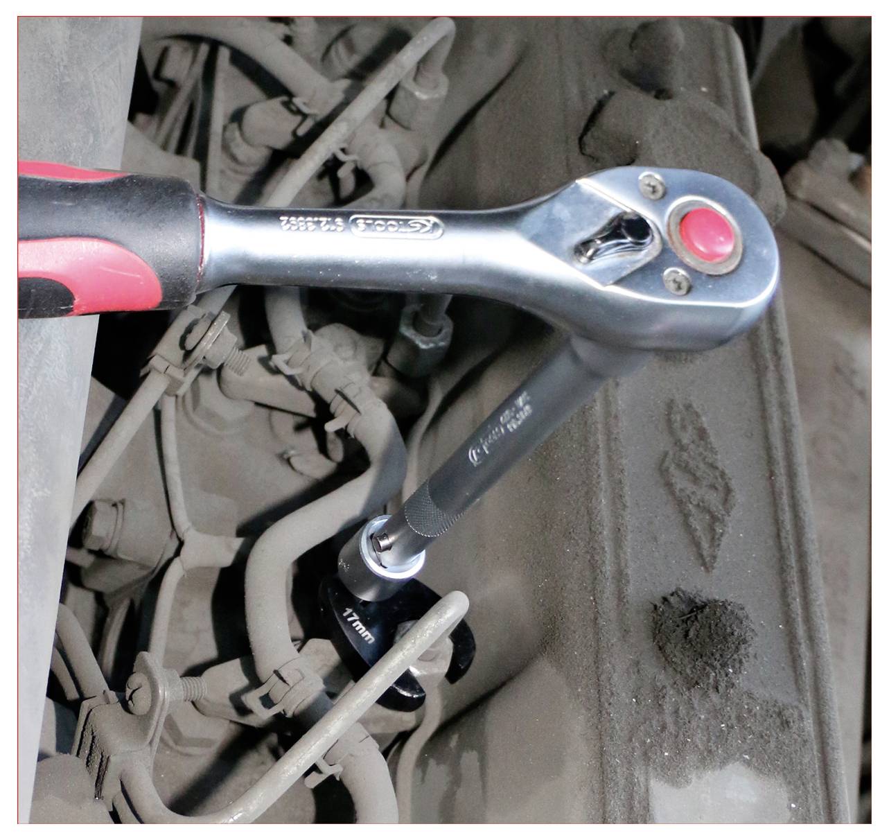 Eine Knarrenschlüssel zieht eine Schraube an einem staubigen Motorenteil fest und demonstriert die Werkzeugverwendung bei der Autoreparatur.