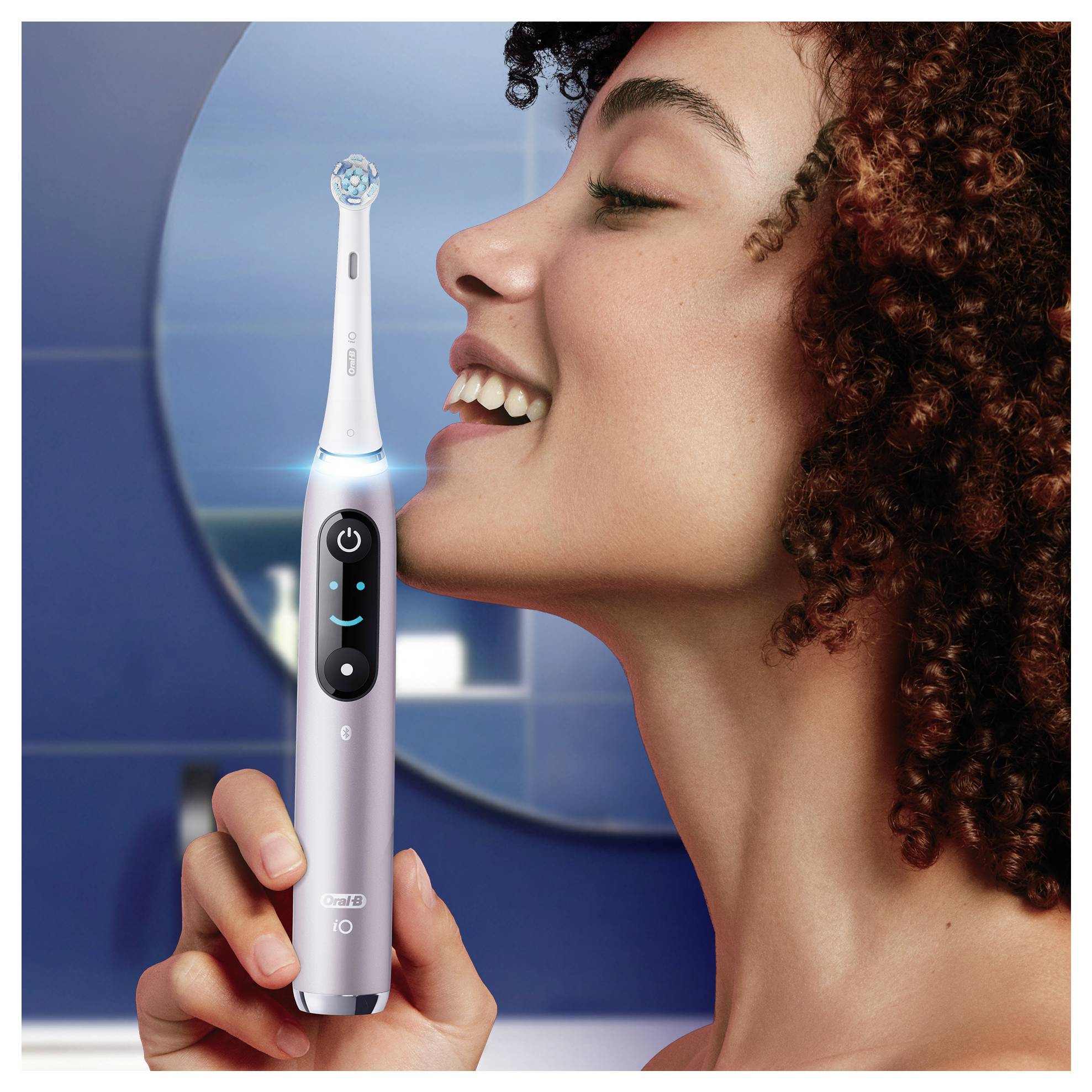 Eine Person, die lächelt und während sie eine elektrische Zahnbürste nahe ihrem Gesicht hält, zeigt deren Gebrauch und betont die Zahnpflege.