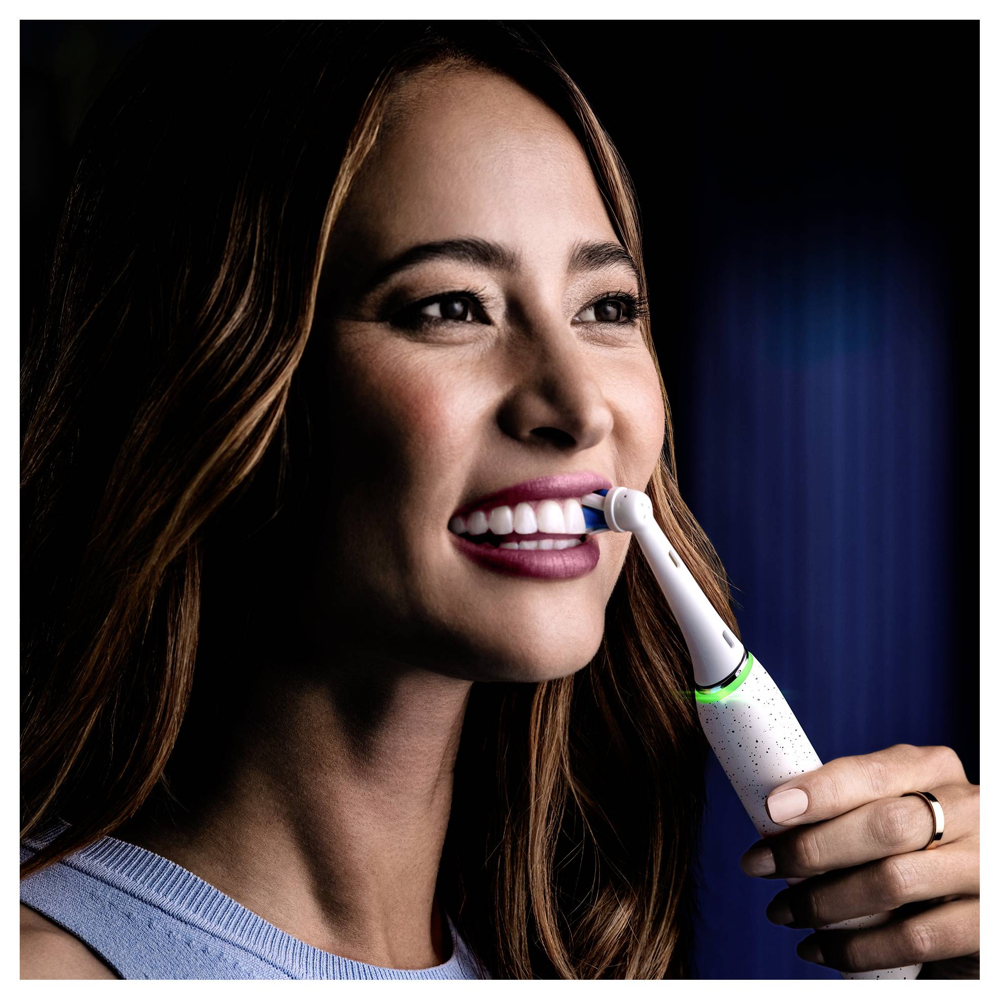 Eine Person mit langen Haaren benutzt eine elektrische Zahnbürste, lächelt und demonstriert Mundhygiene. Die Zahnbürste verfügt über einen leuchtenden Indikator.