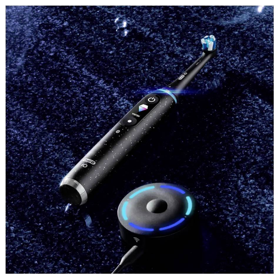 Eine elektrische Zahnbürste mit beleuchteten Tasten ruht auf einer glänzend schwarzen Oberfläche neben einer kreisförmigen Ladestation.