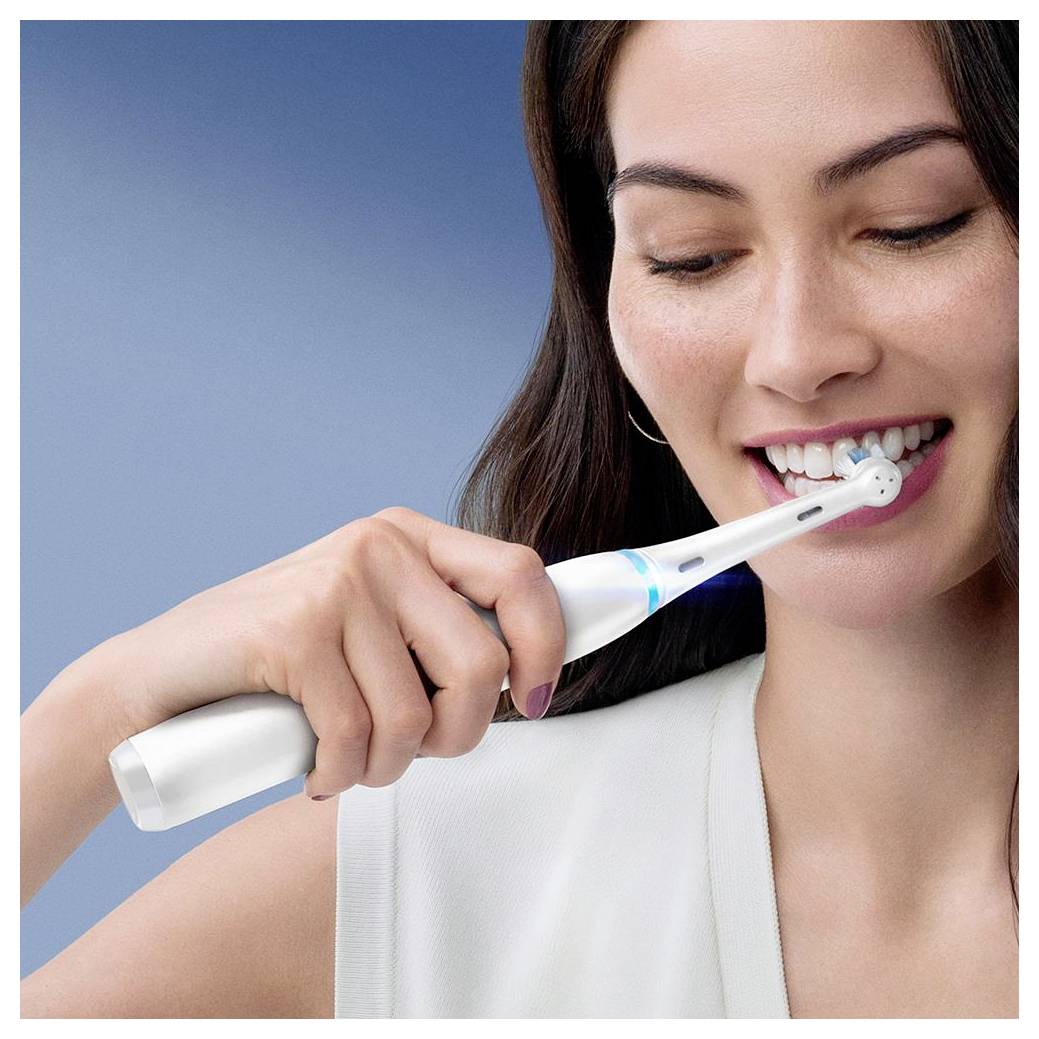 Eine Person benutzt eine elektrische Zahnbürste und lächelt während des Zähneputzens in einem hell erleuchteten Raum.