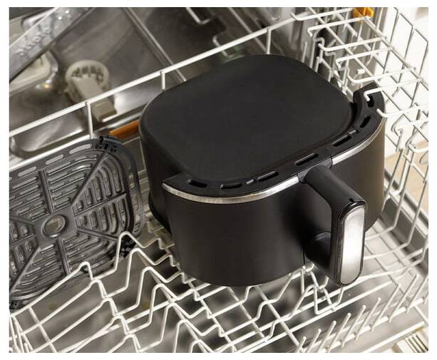 Ein Heißluftfritteuse-Korb und -Tablett werden in einer Spülmaschine platziert, was darauf hinweist, dass sie gereinigt werden.