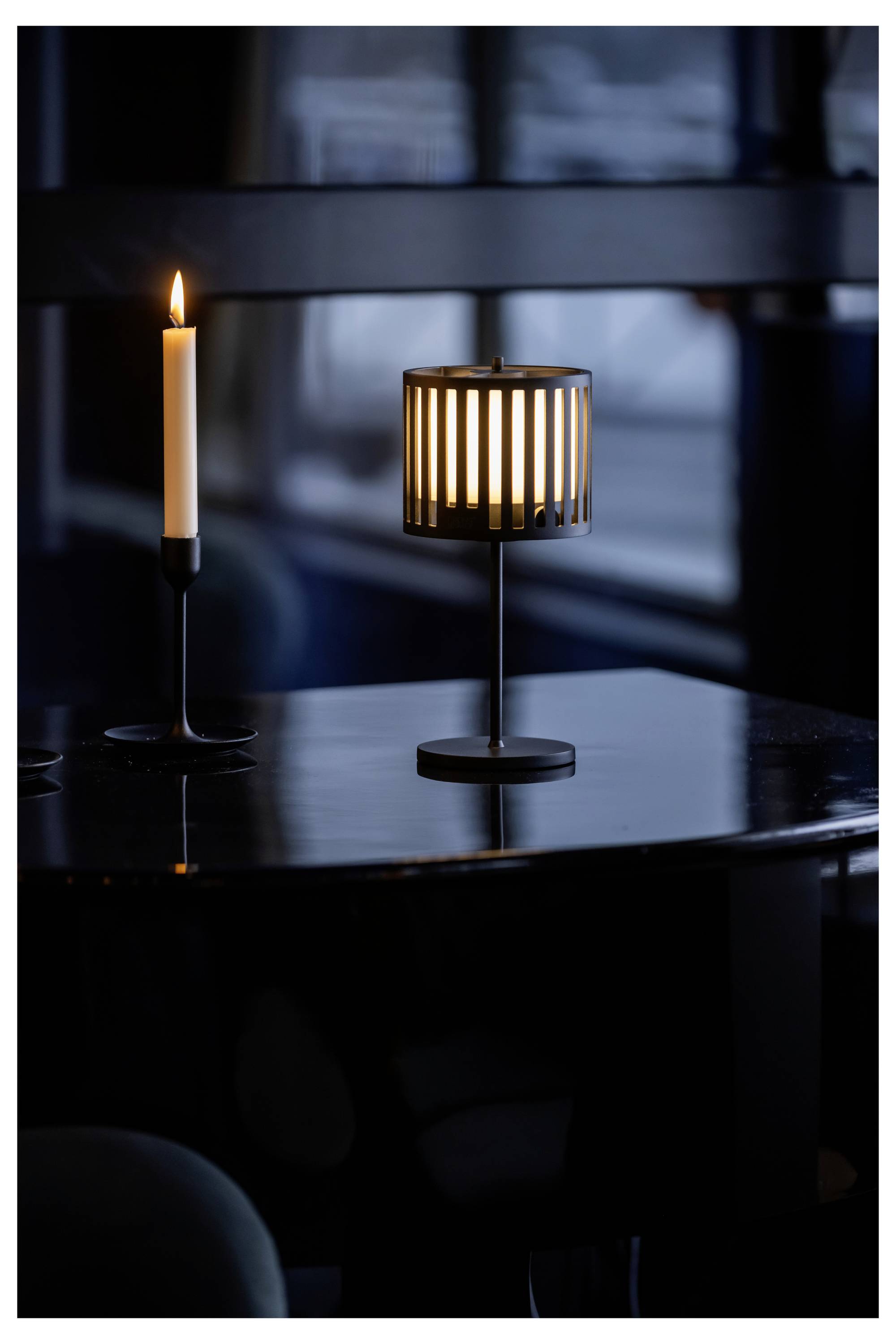 Ein schwach beleuchteter Esstisch mit einer Kerze in einem Kerzenhalter und einer kleinen Lampe, die eine intime und gemütliche Atmosphäre erzeugen.