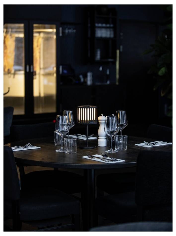 Ein schwach beleuchteter Restauranttisch für vier Personen, mit Weingläsern, Wassergläsern, Besteck und einer beleuchteten Dekorationslampe in der Mitte.