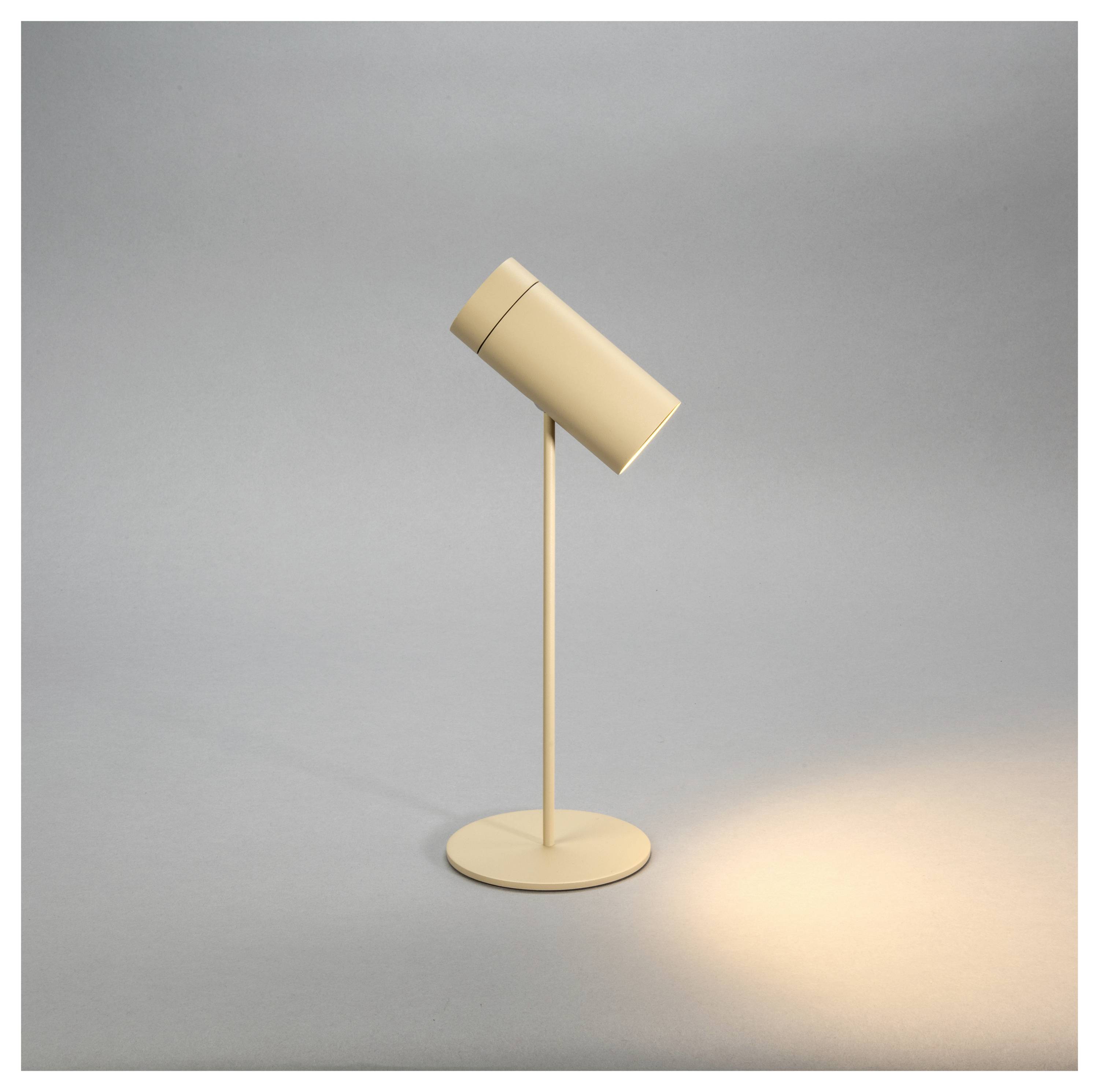 Eine elegante, moderne beige Tischlampe mit einem zylindrischen Lampenschirm projiziert Licht auf eine graue Oberfläche und erzeugt einen weichen, gezielten Schein.