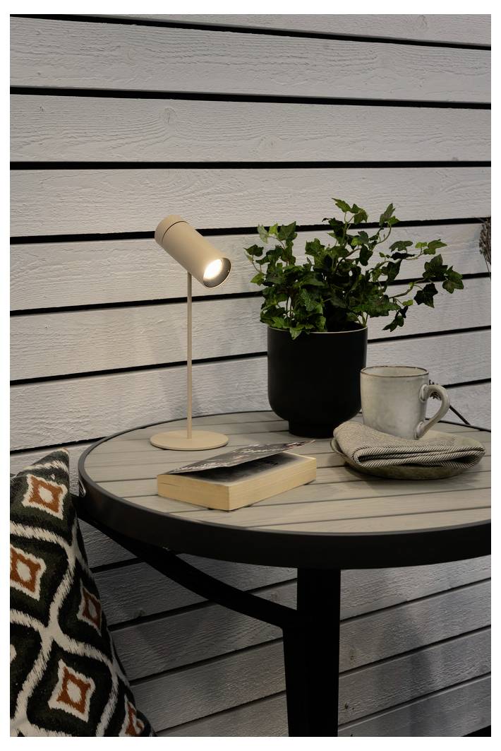 Ein kleiner runder Tisch mit einer Topfpflanze, einem Buch, einer Tasse und einem zusammengelegten Tuch steht auf einer Holzterrasse vor einer horizontal verschalten Wand.