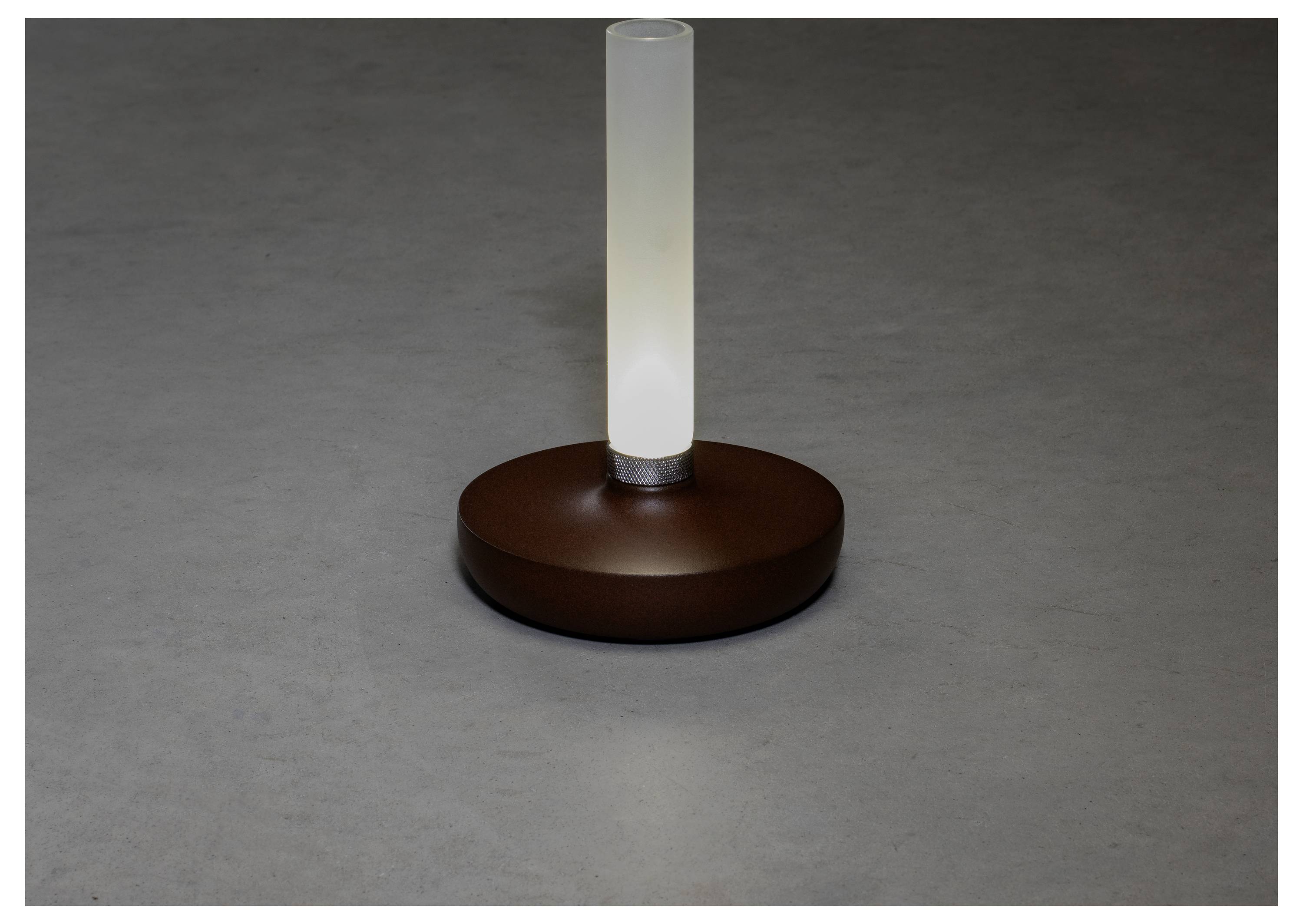 Eine moderne Tischlampe mit einer zylindrischen, matten Glühbirne auf einer runden braunen Basis, die in einem dunkel beleuchteten Raum ein subtiles Leuchten verbreitet.