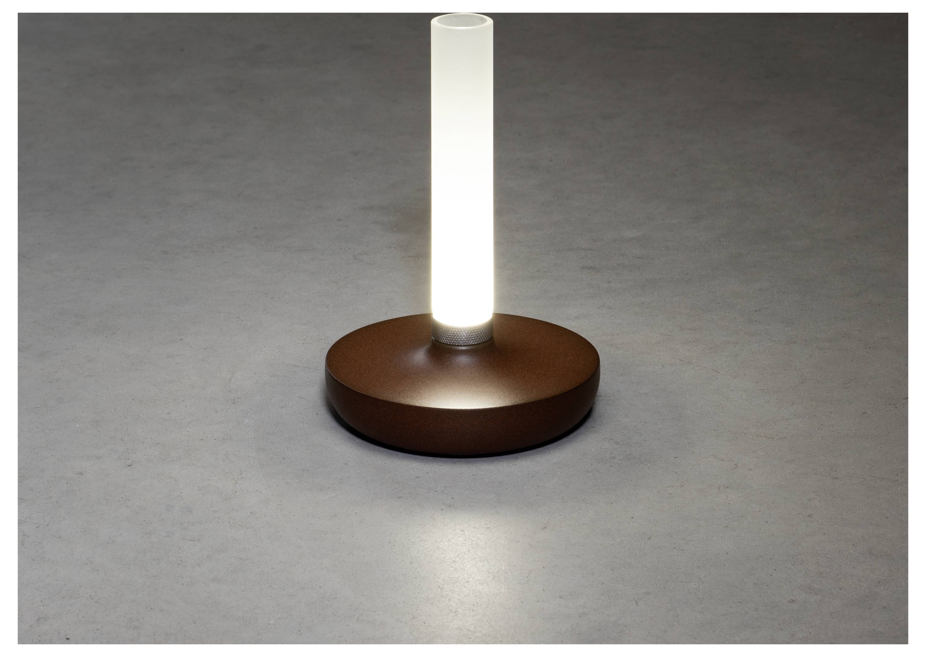 Eine zylindrische weiße Lampe auf einer runden braunen Basis, die auf einer glatten grauen Oberfläche leuchtet.