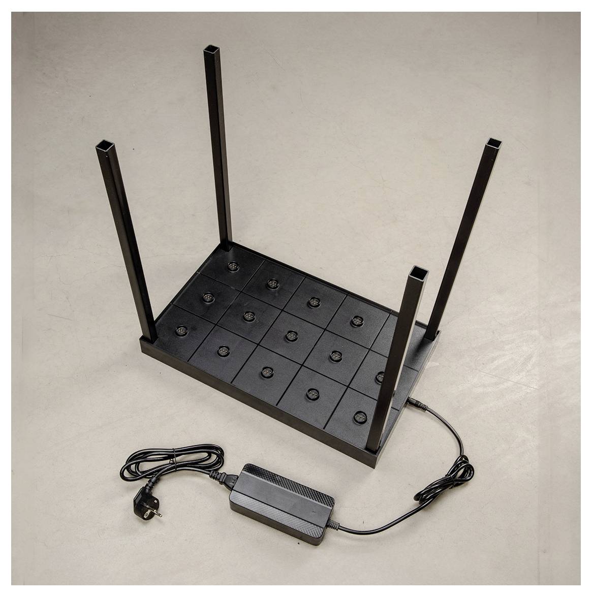 Ein Metallrahmen mit vier vertikalen Stäben, die an einer quadratischen Basis befestigt sind und ein Raster aus schwarzen Knöpfen aufweisen, der mit einem Netzteil verbunden ist.