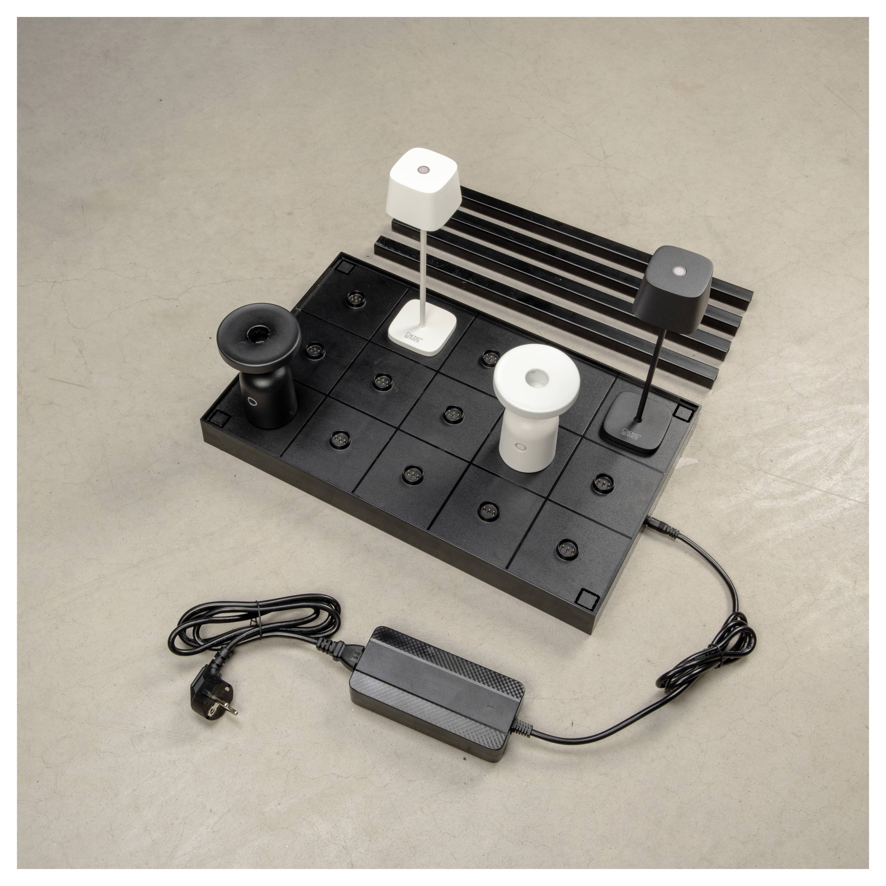 Eine Präsentation verschiedener moderner Schreibtischlampen in Schwarz und Weiß, ausgestellt auf einem modularen Brett mit angeschlossenem Netzteil.