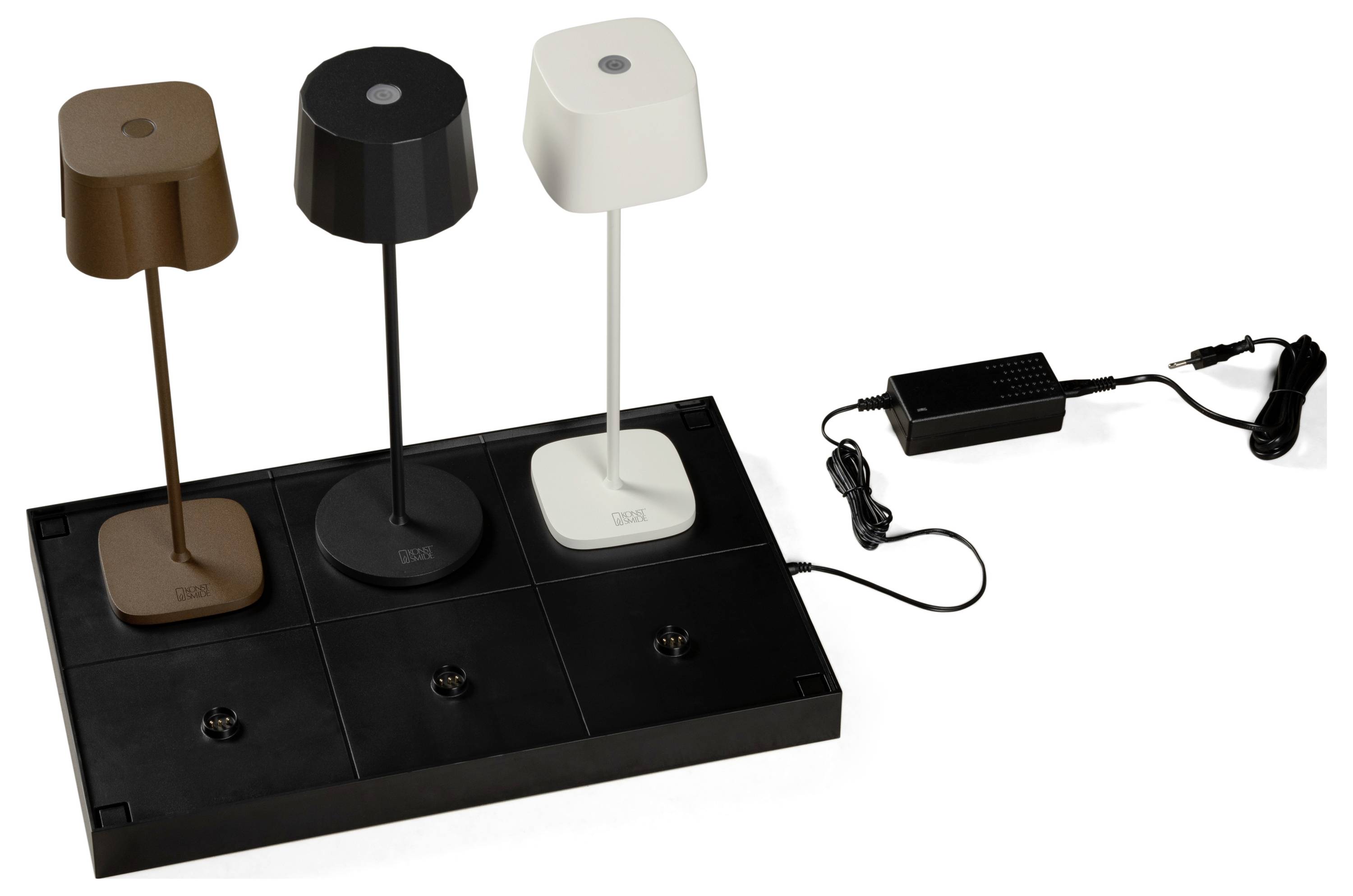 Drei Tischlampen in Braun, Schwarz und Weiß werden auf einer schwarzen Basis ausgestellt, mit einem Netzteil verbunden und präsentieren dabei Farbe und Design.