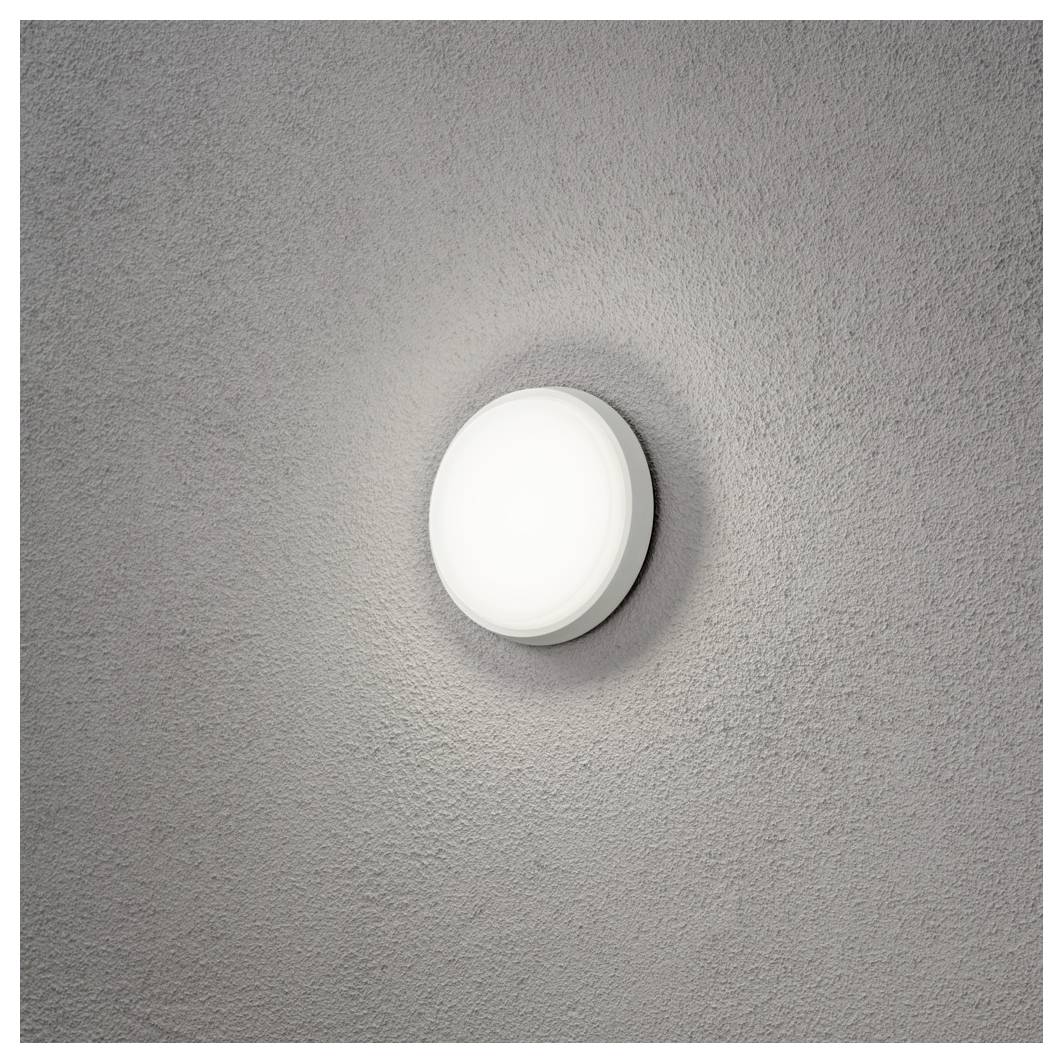 Eine runde, wandmontierte Leuchte mit einer satinierten Abdeckung, die ein weiches Leuchten vor einem strukturierten grauen Hintergrund abstrahlt.