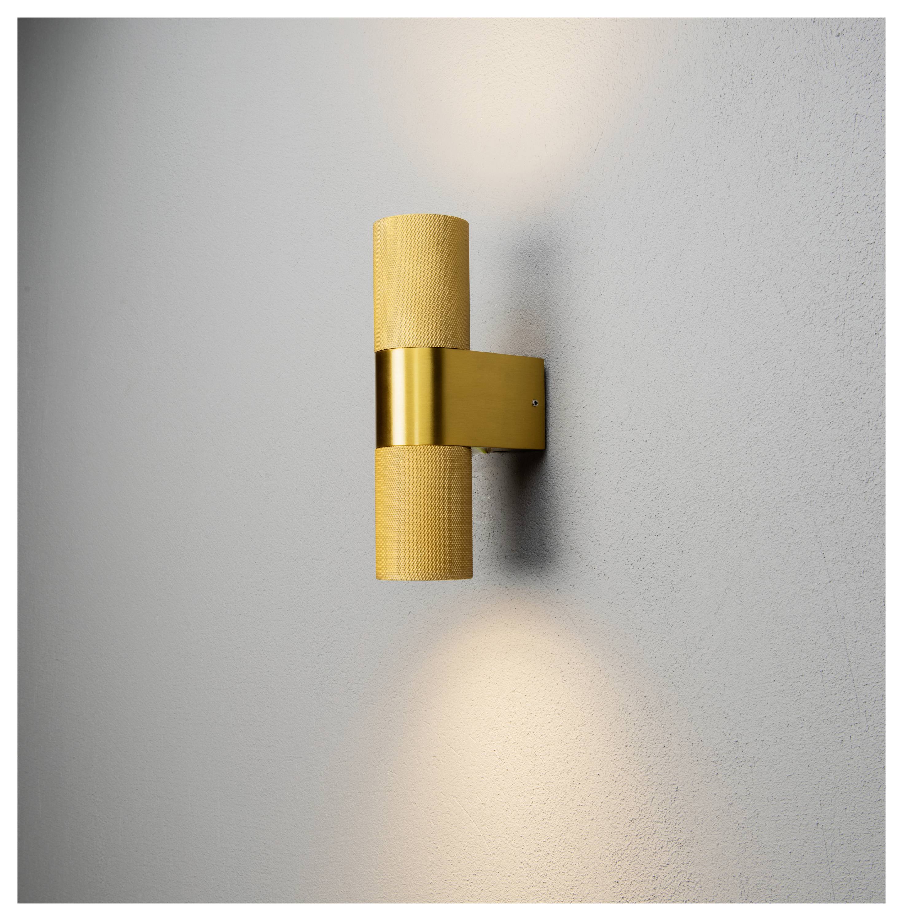 Goldene zylindrische Wandleuchte mit zwei Lichtquellen, die Licht sowohl nach oben als auch nach unten an einer grauen Wand ausstrahlt.