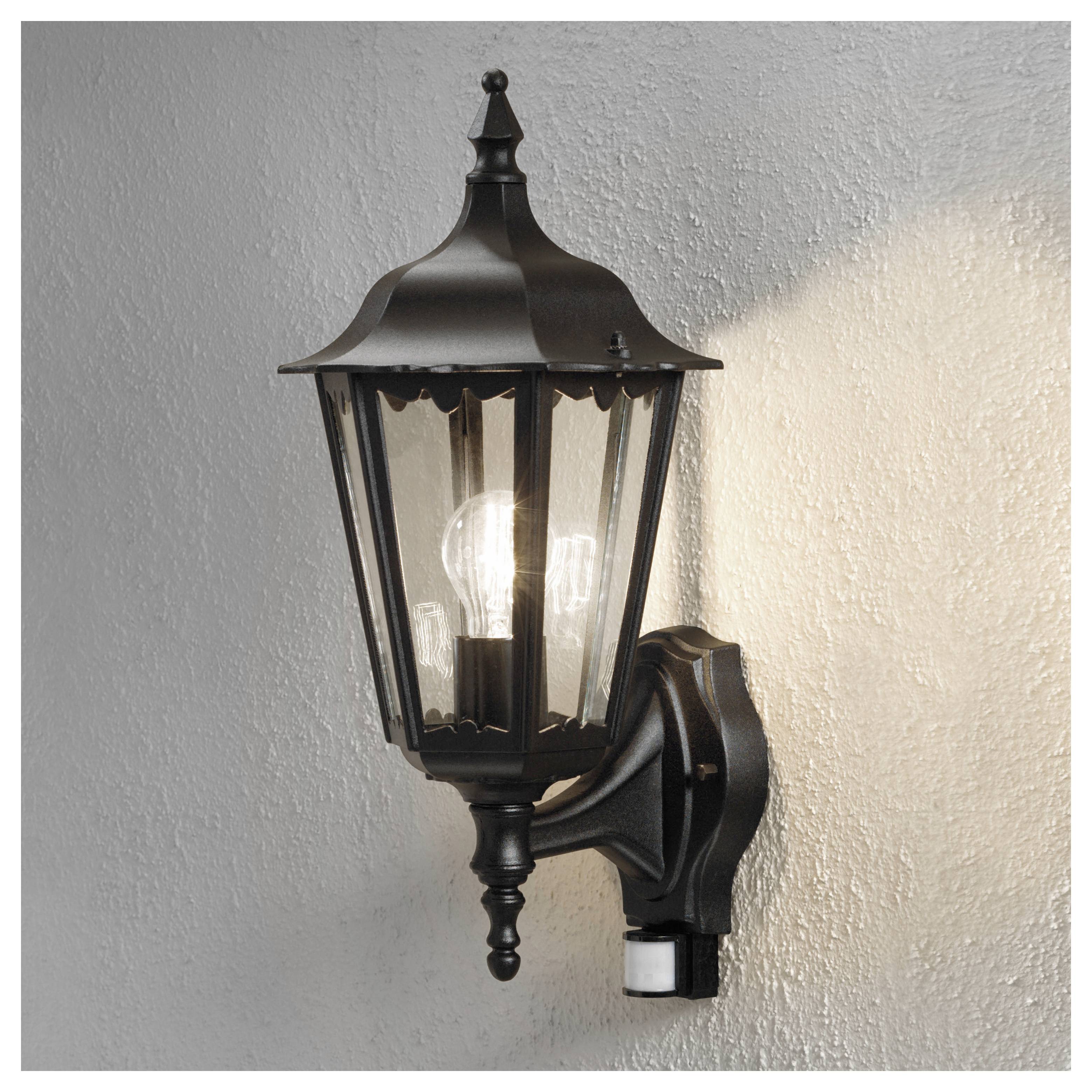 Eine schwarze, im Vintage-Stil gehaltene Laterne, an einer Wand befestigt, mit einer leuchtenden Glühbirne im Inneren, die die umgebende strukturierte Oberfläche beleuchtet.